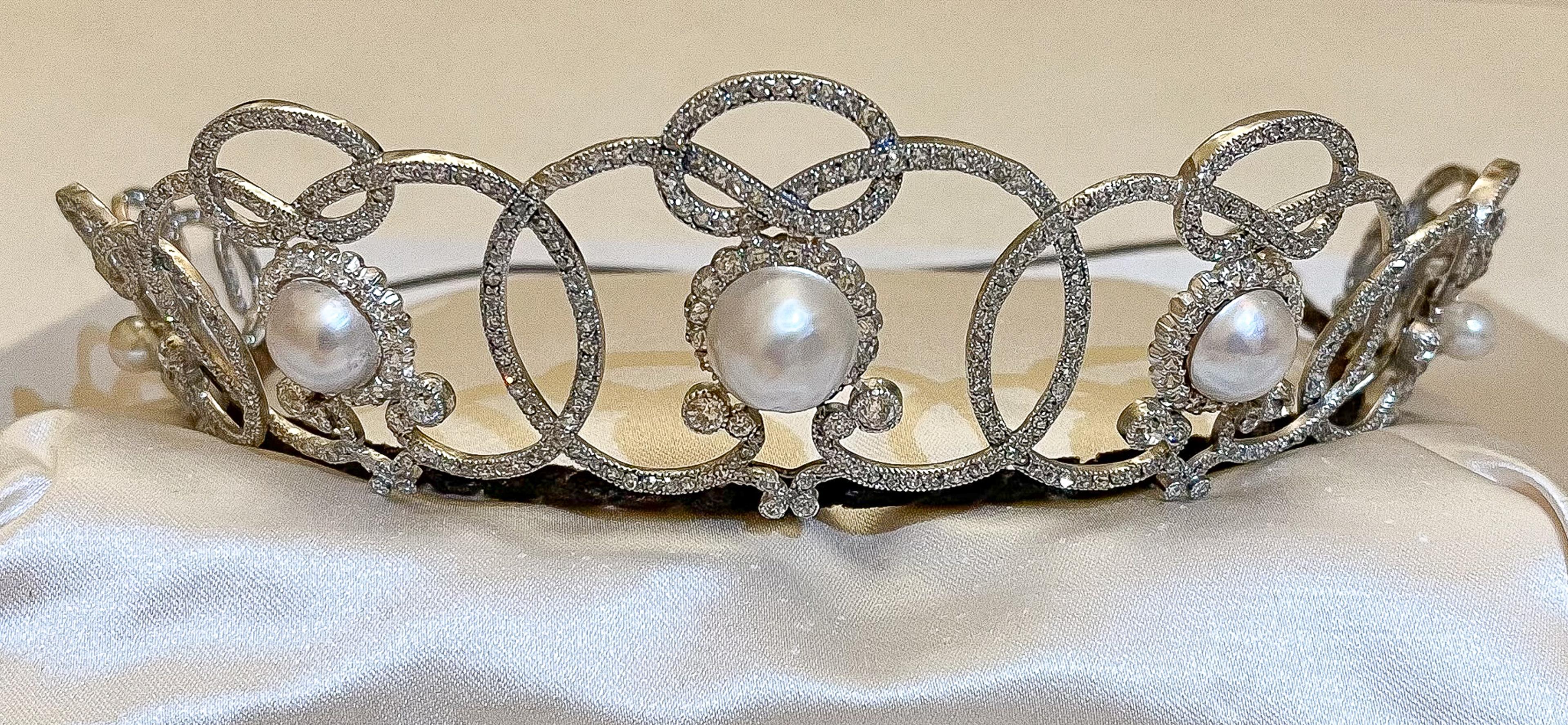 Et diadem med sløyfer av diamanter og store perler ligger på et kremfarget tøy.