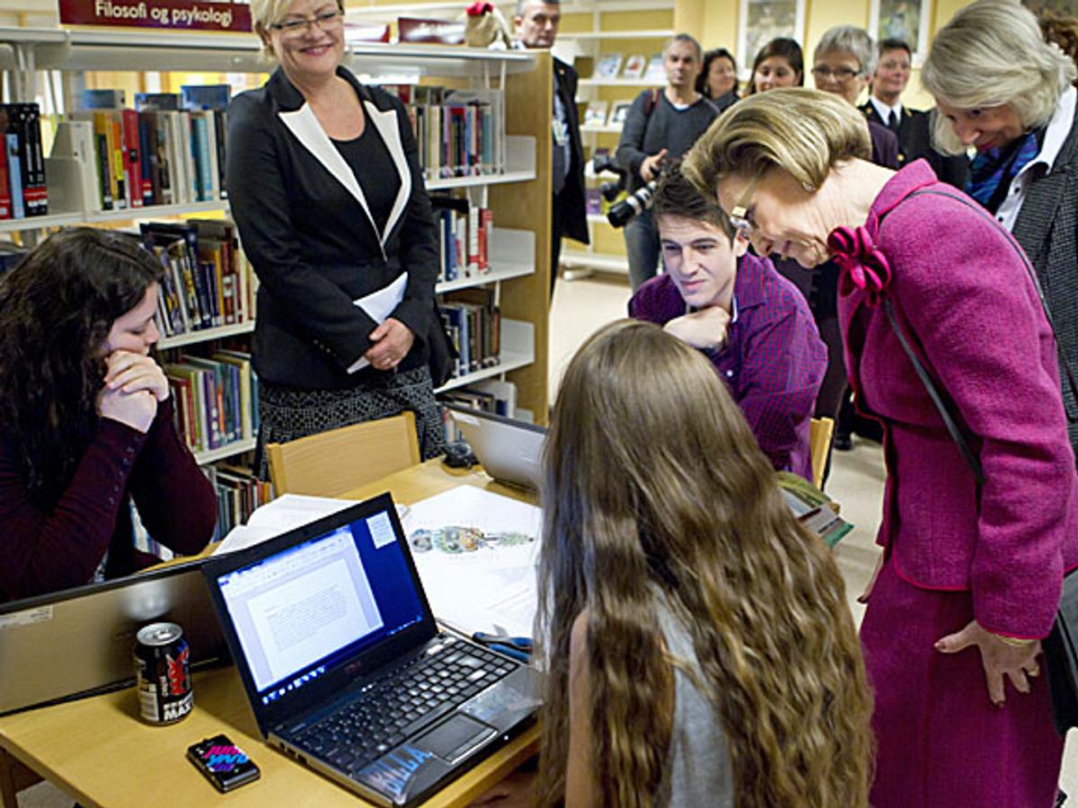 Dronning Sonja ser ned på en elev som sitter ved en PC sammen med to andre medelever.