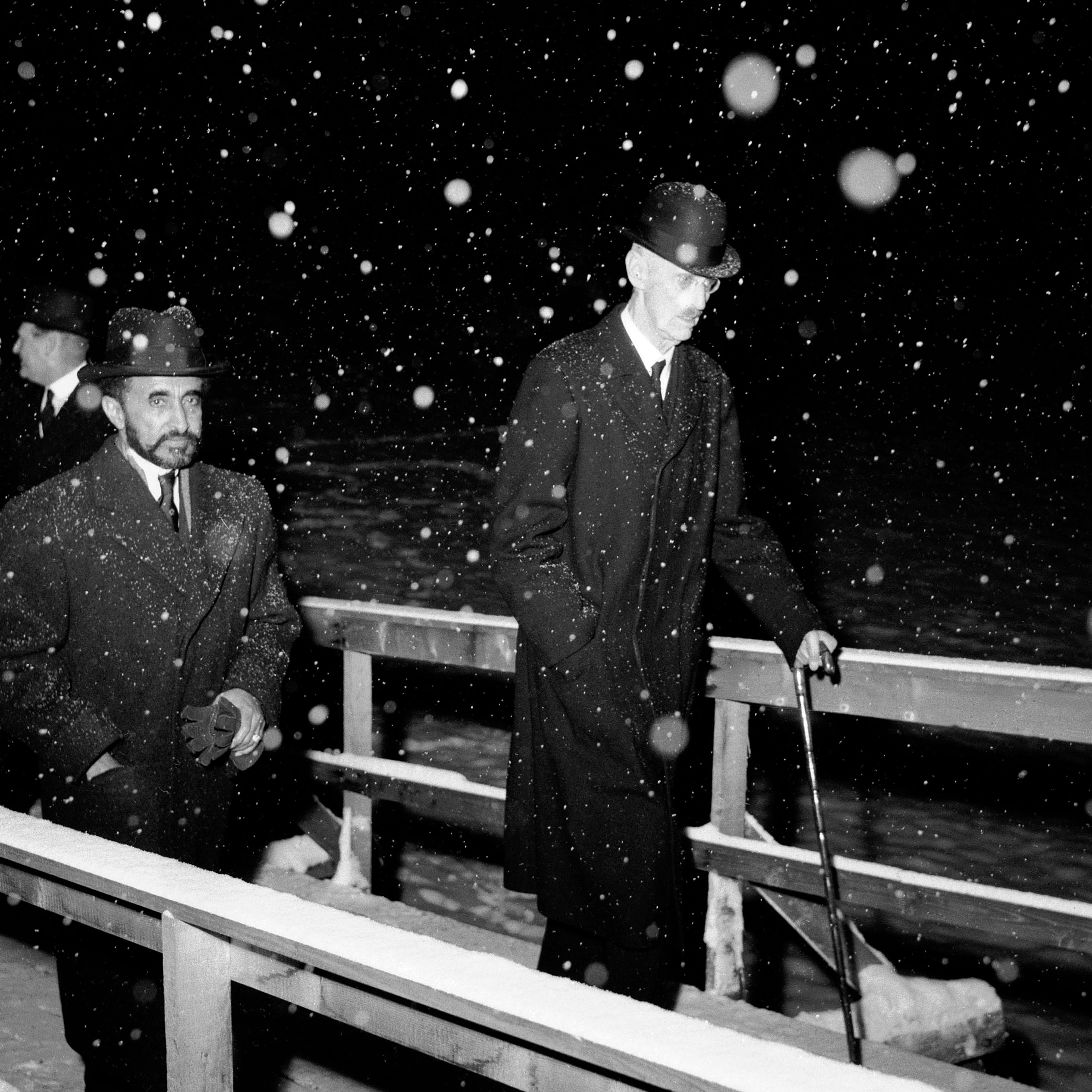 Sort-hvittbilde av Kong Haakon og Keiseren som går opp en rampe. Det er mørkt og snør tett.