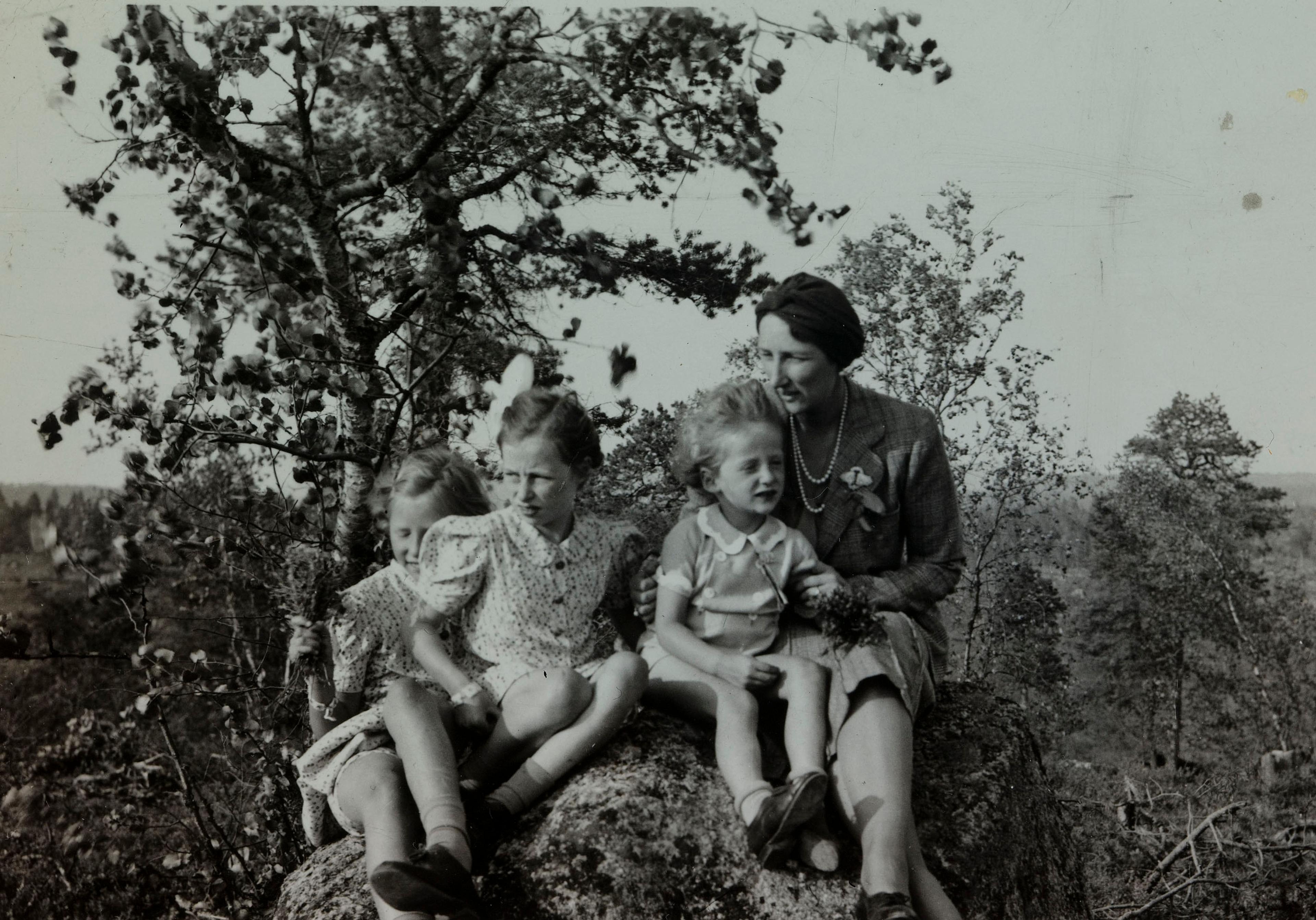 Kronprinsesse Märtha sitter sammen med barna på en stein. Sommerlige klær.
