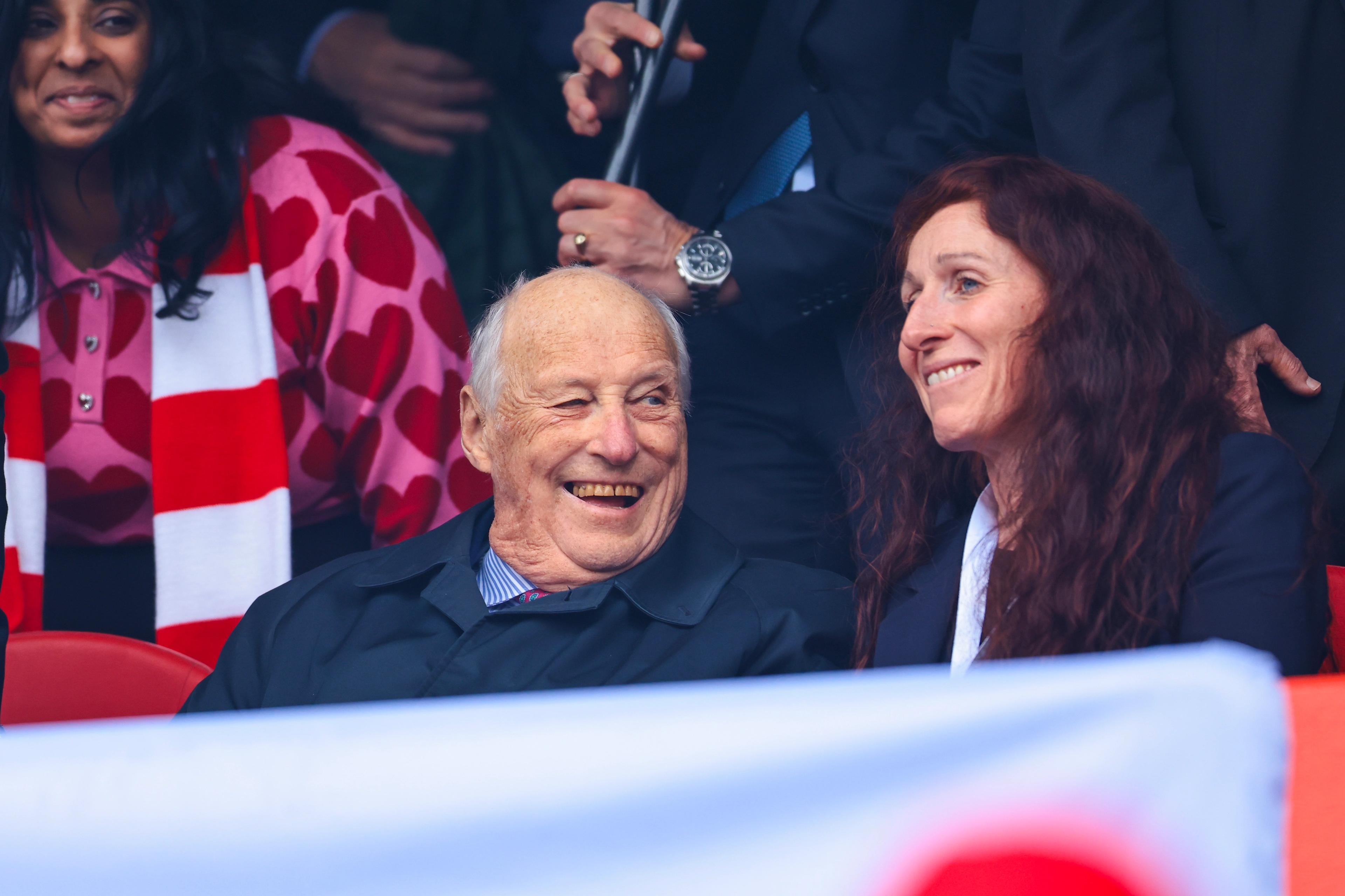 Kong Harald og Lise Klaveness smiler bredt fra tribunen.