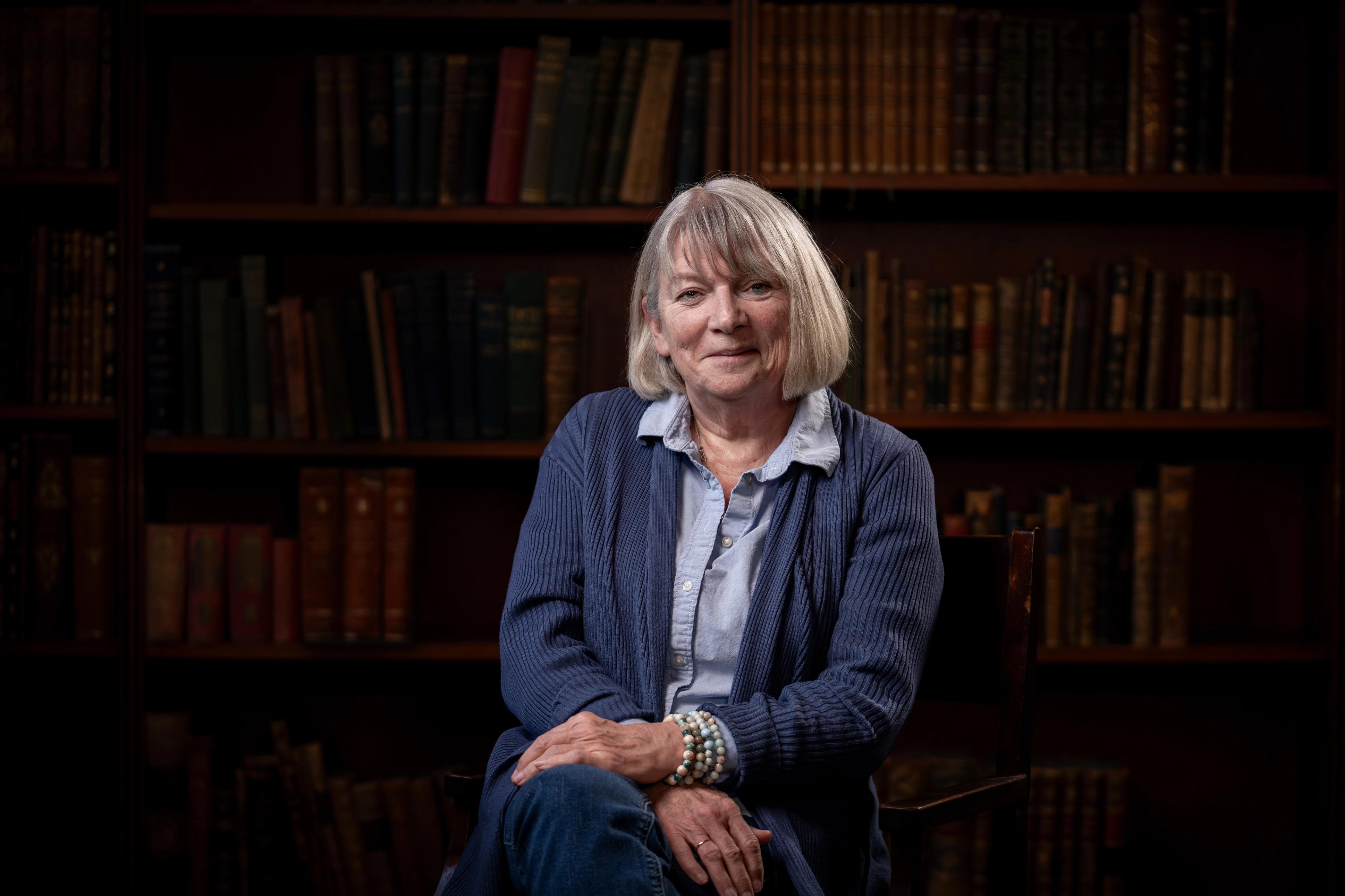 Paula Stevens sit smilande framfor ei bokhylle full av bøker.