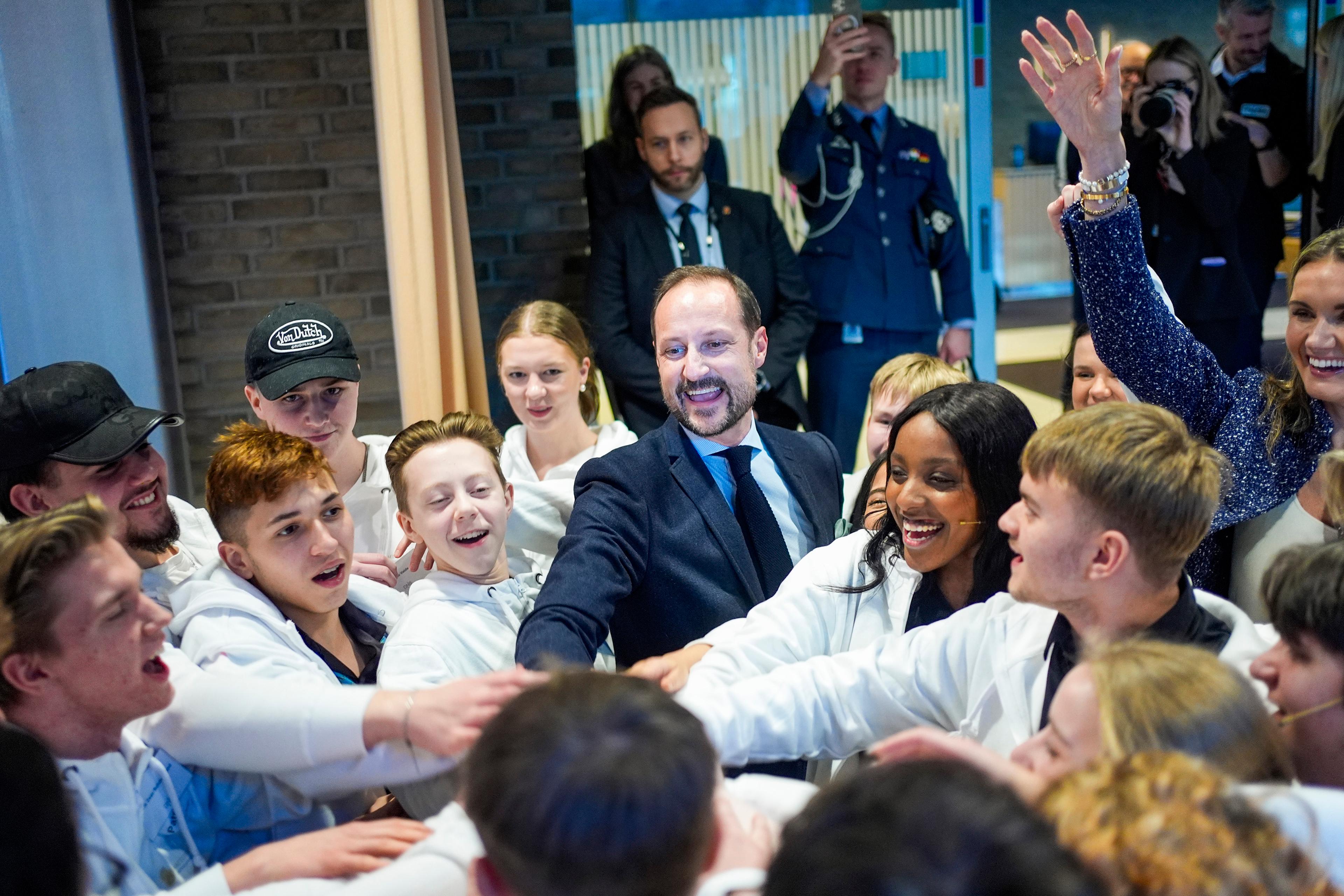 Kronprins Haakon med en gruppe leende ungdommer.