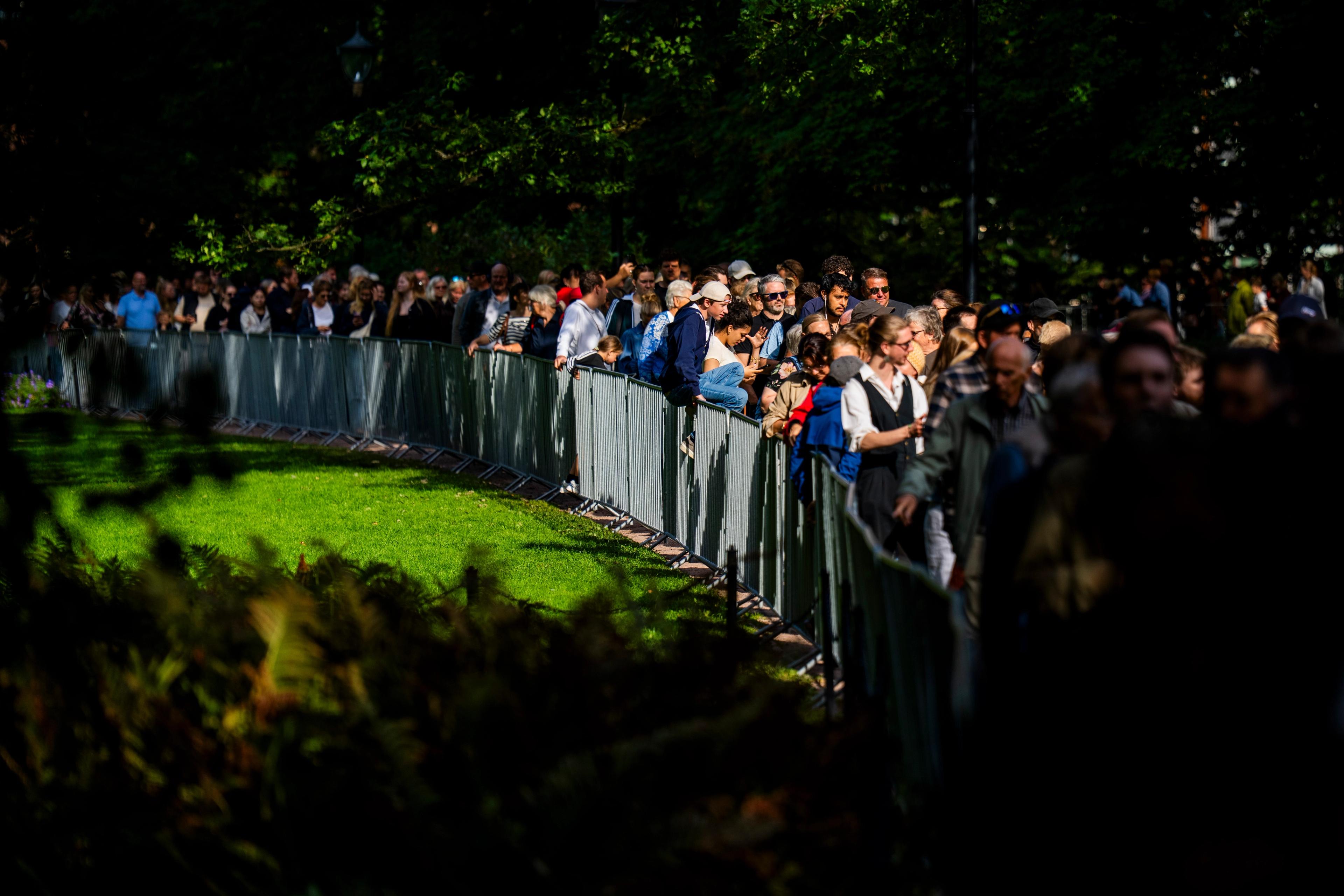 En stor mengde mennesker står i kø langs et gjerde i Slottsparken.