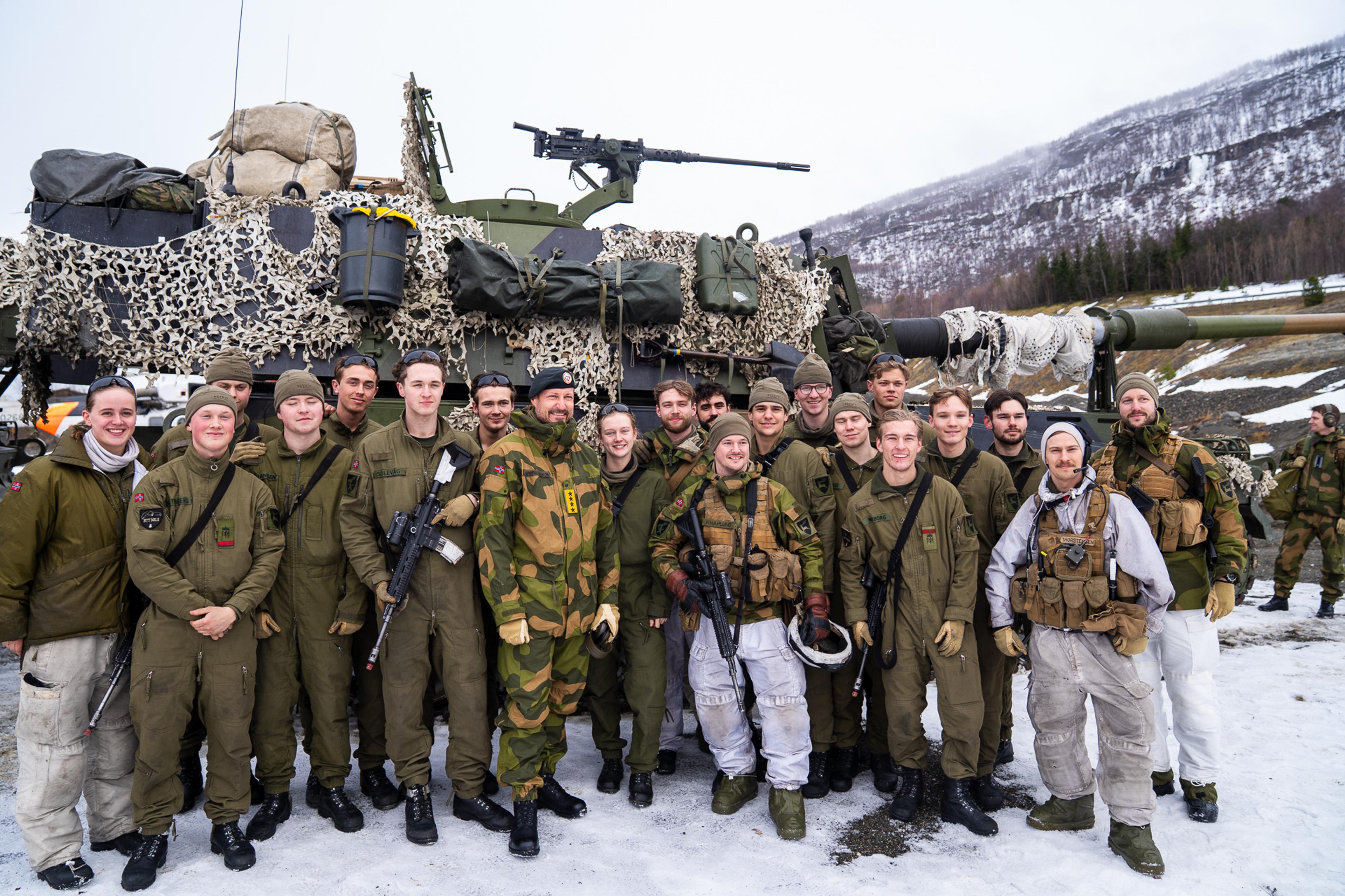 Kronprins Haakon med en mengde norske soldater rundt seg, står foran en artillerivogn under øvelse Cold Response 2026.