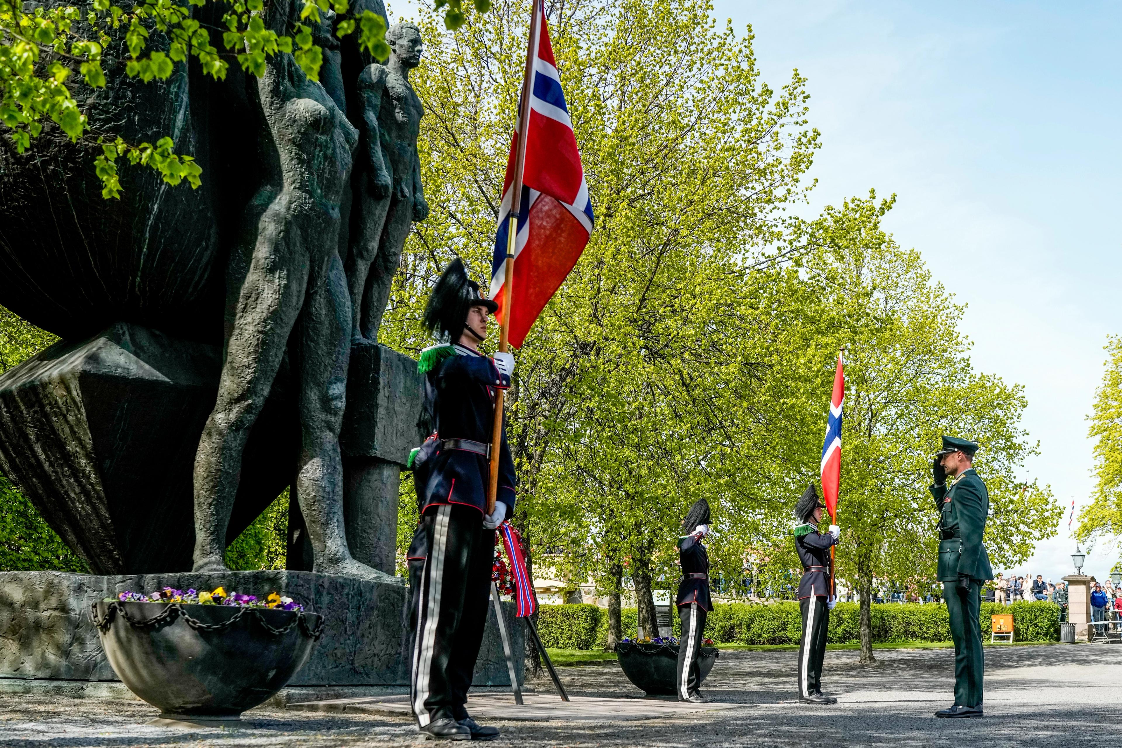 Kronprins Haakon gjør honnør til lua. To gardister står flaggvakt på kvar side.