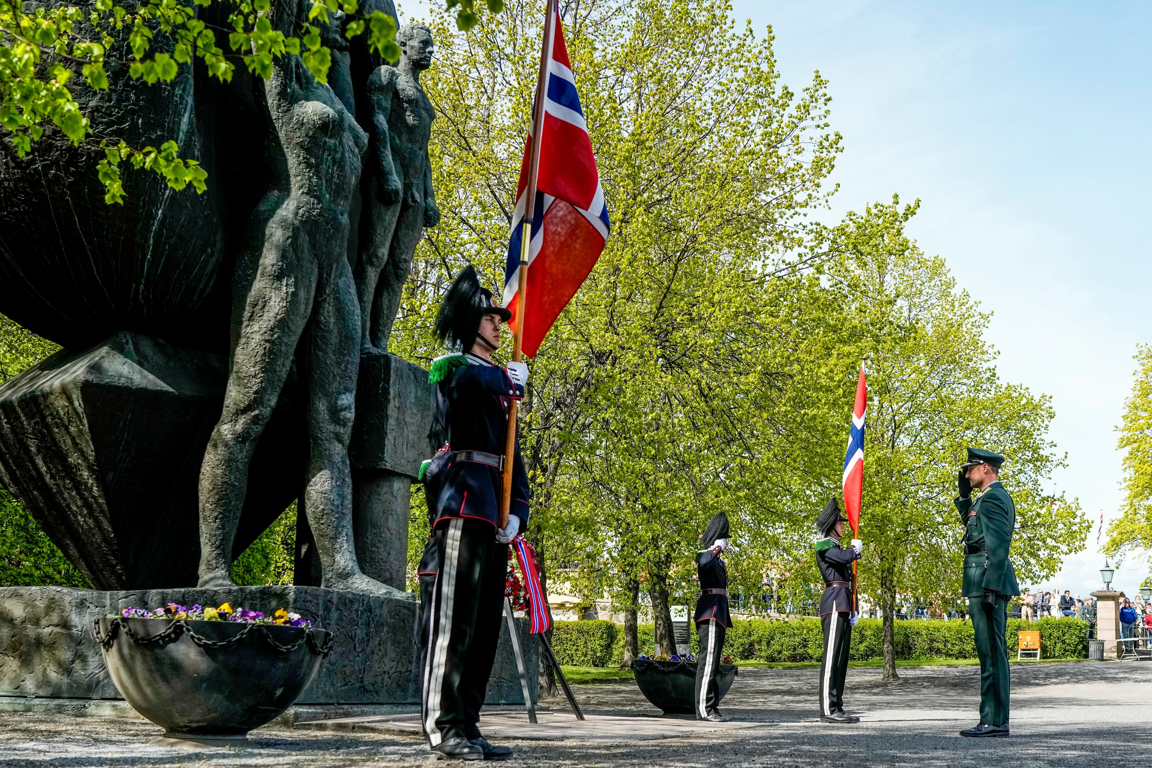 Kronprins Haakon gjør honnør til lua. To gardister står flaggvakt på kvar side.