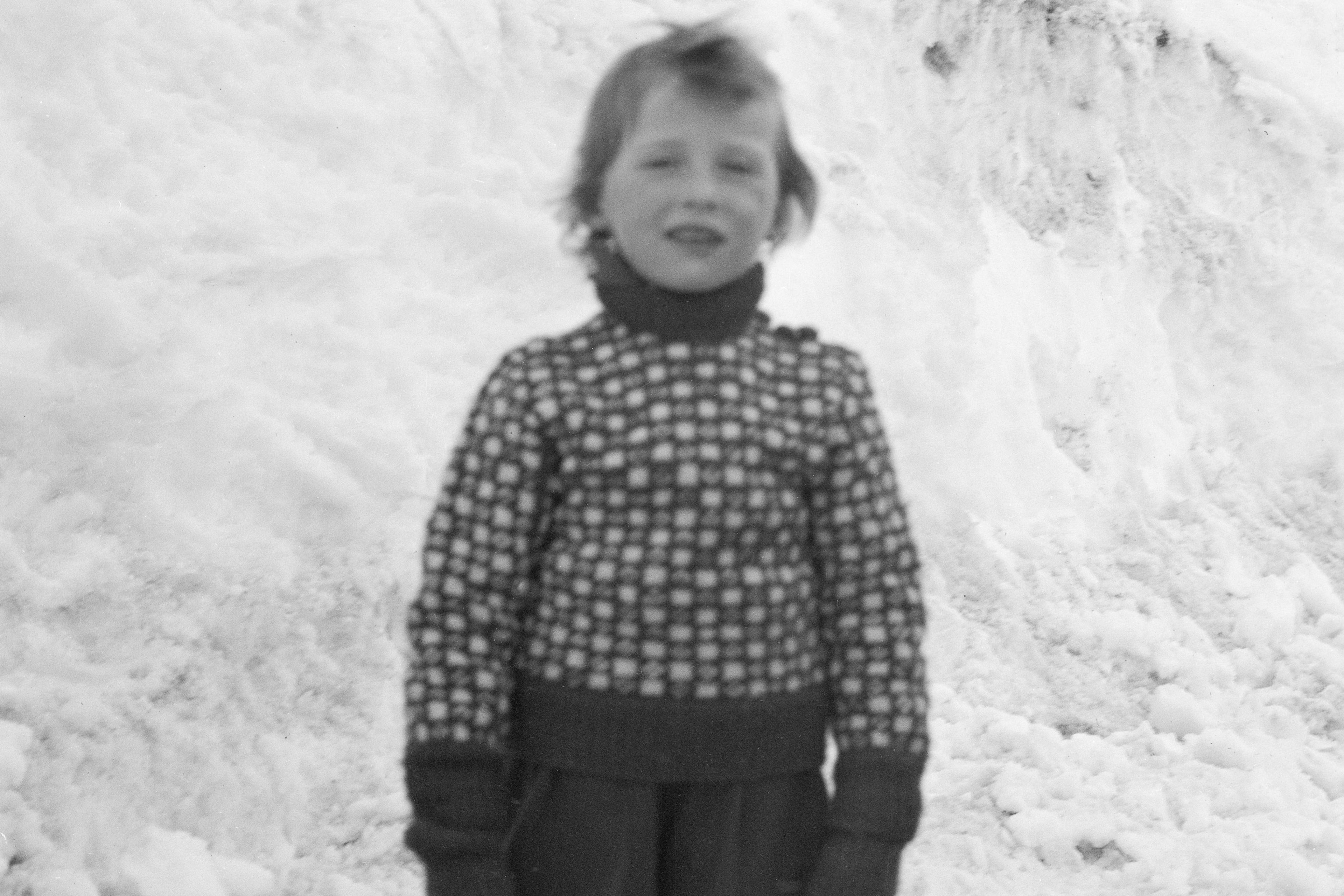 Prins Harald i strikkegenser og votter, foran en vegg av snø.