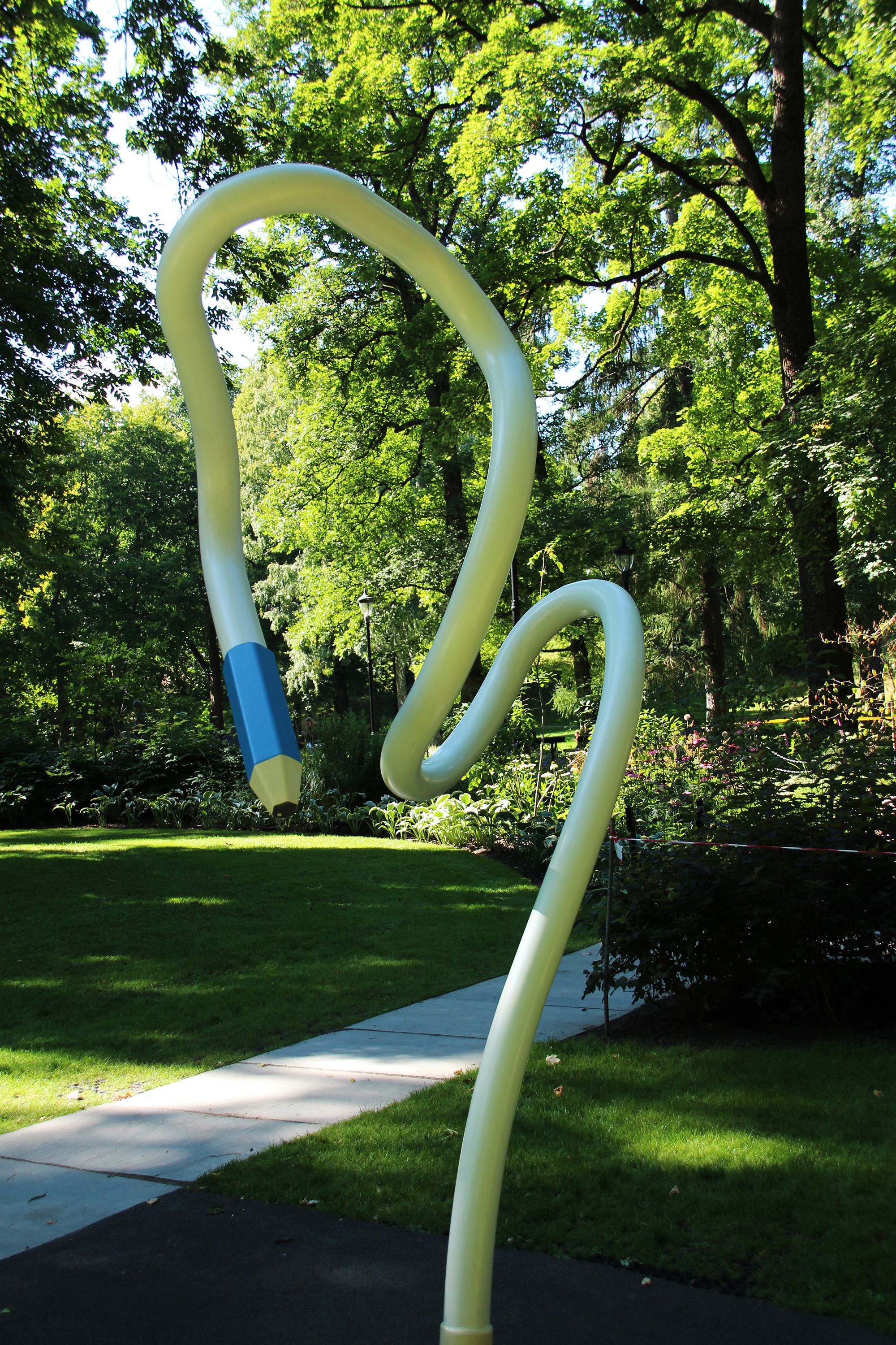 En hvit blyant kommer opp av bakken og bukter seg høyt opp i luften. Den svinger ned igjen, slik at tuppen - en blå blyantspiss -  er omtrent i høyde med den som ser.