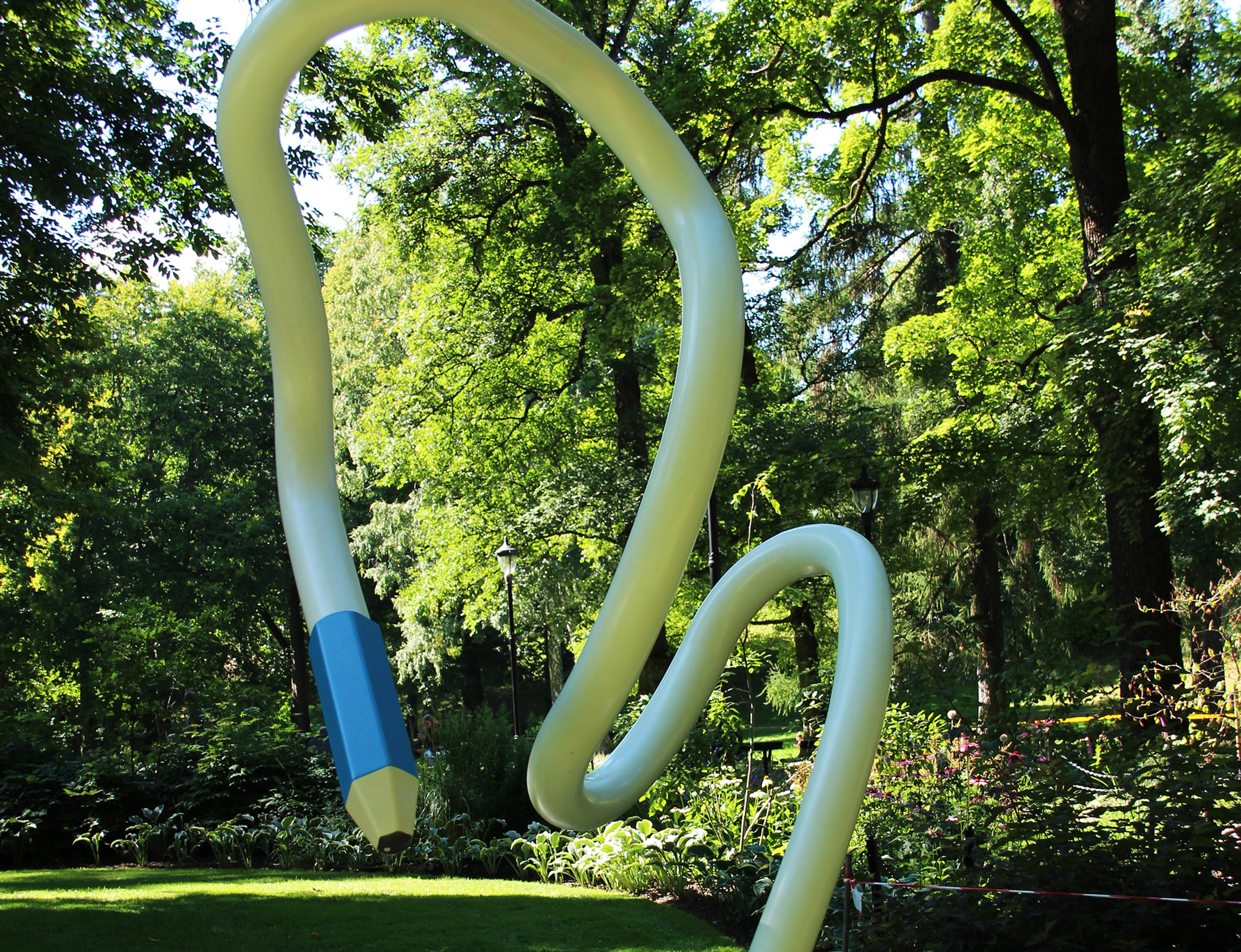 En hvit blyant kommer opp av bakken og bukter seg høyt opp i luften. Den svinger ned igjen, slik at tuppen - en blå blyantspiss - er omtrent i høyde med den som ser.