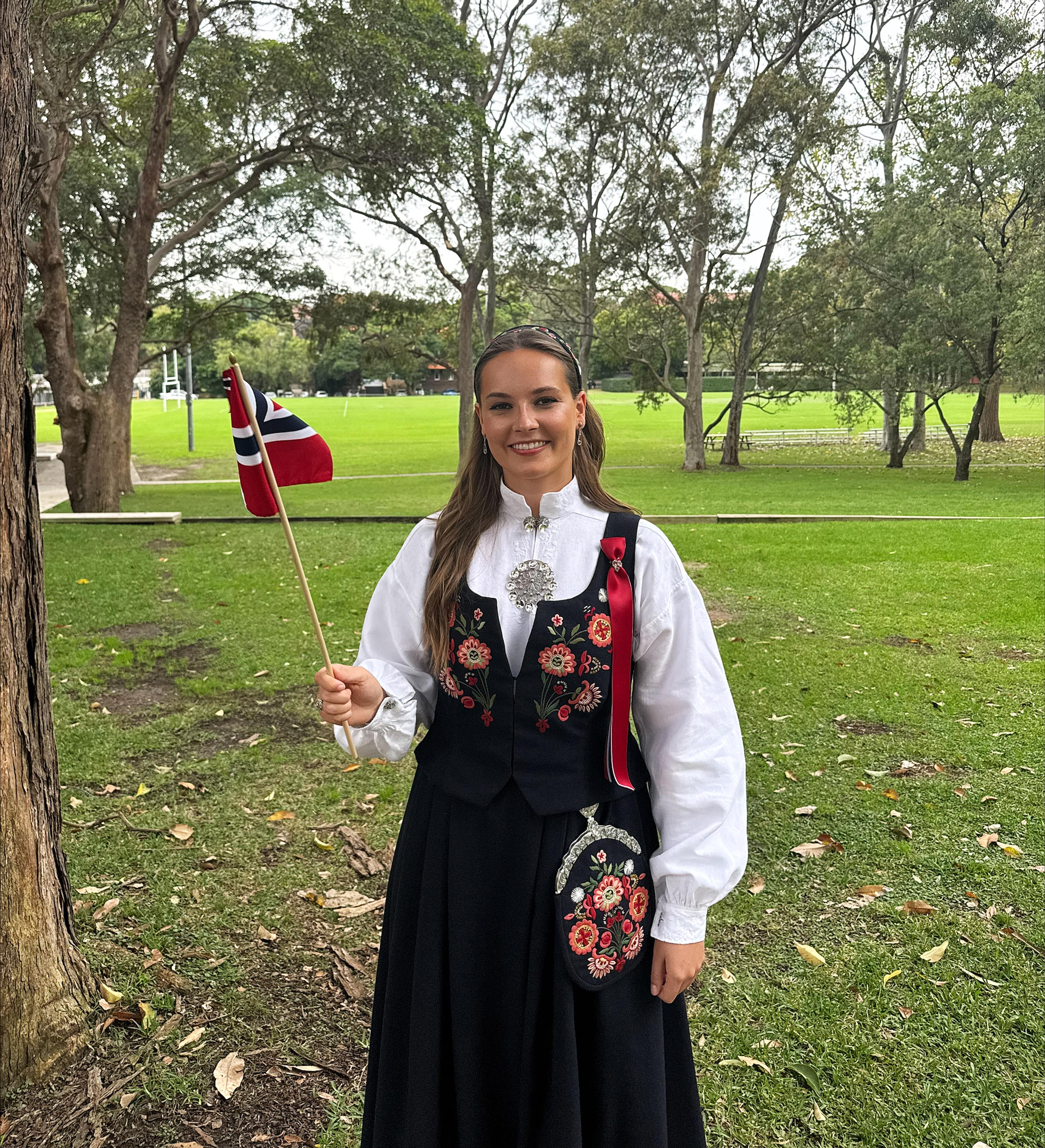 Prinsessen står med flagg og bunad ute i en park.