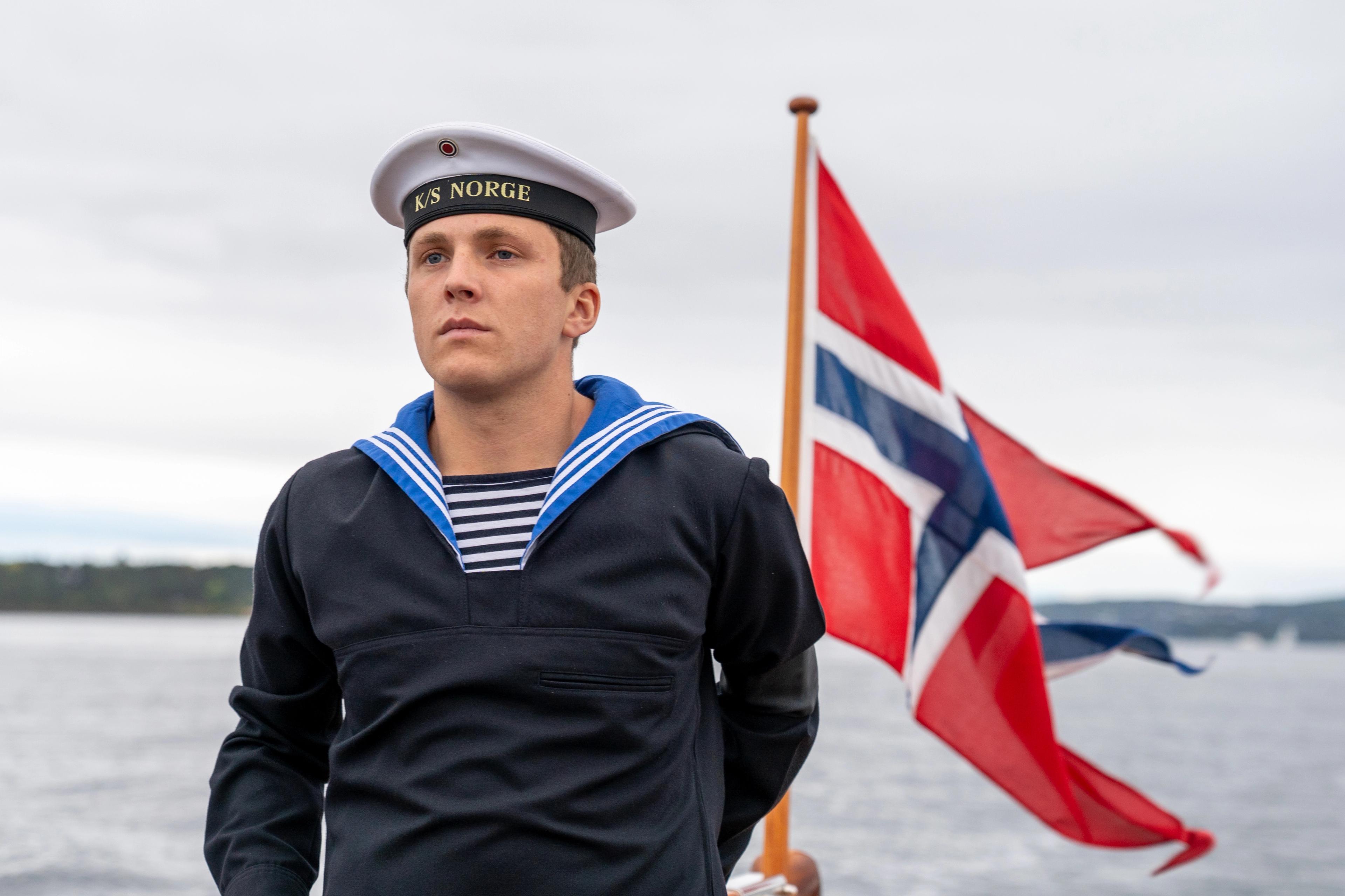 Vernepliktig står om bord sjaluppen med det norske flagget bak.