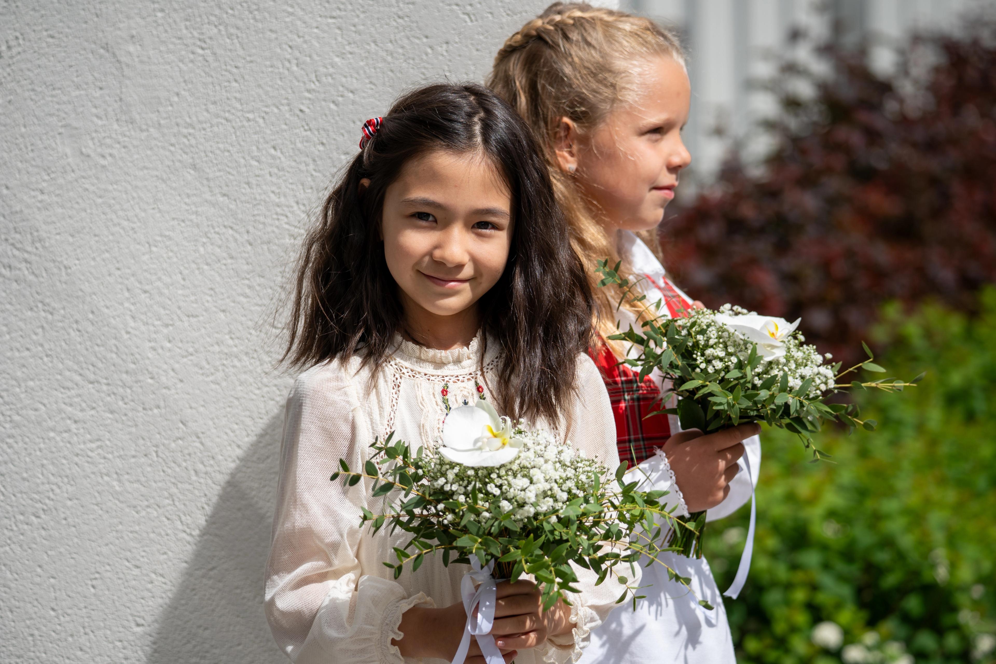 Jenny ser rett i kamera mens hun holder i blomsterbukett i hendene.
