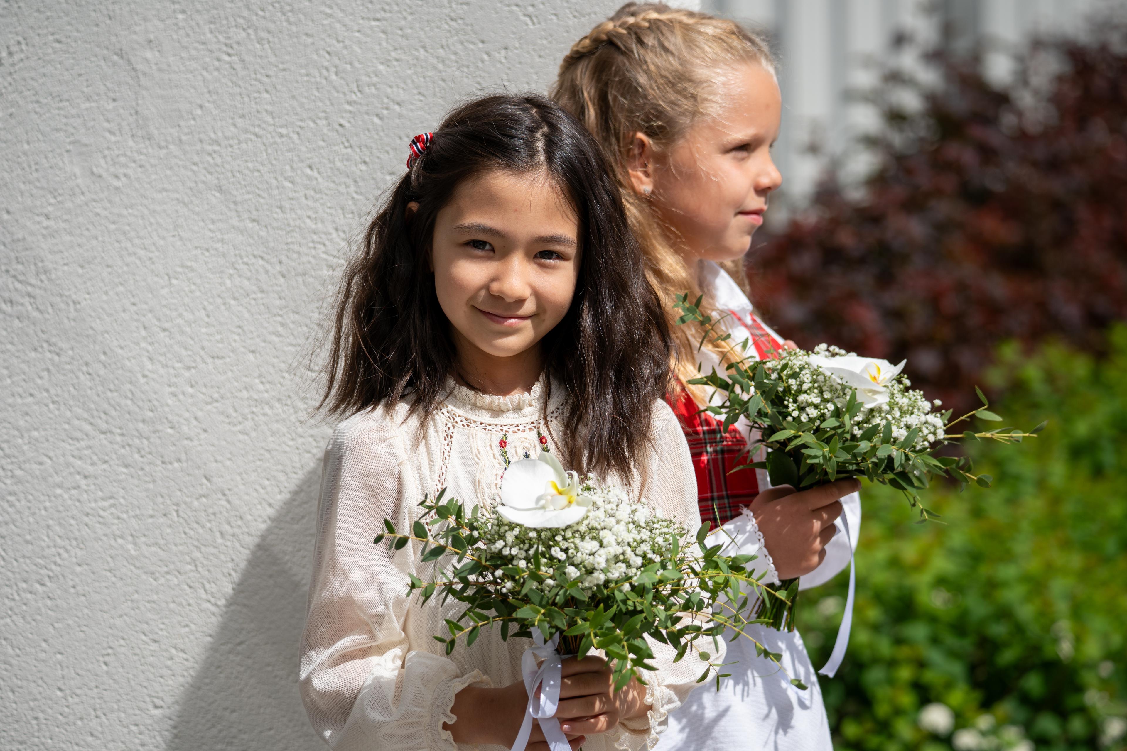 Jenny ser rett i kamera mens hun holder i blomsterbukett i hendene.