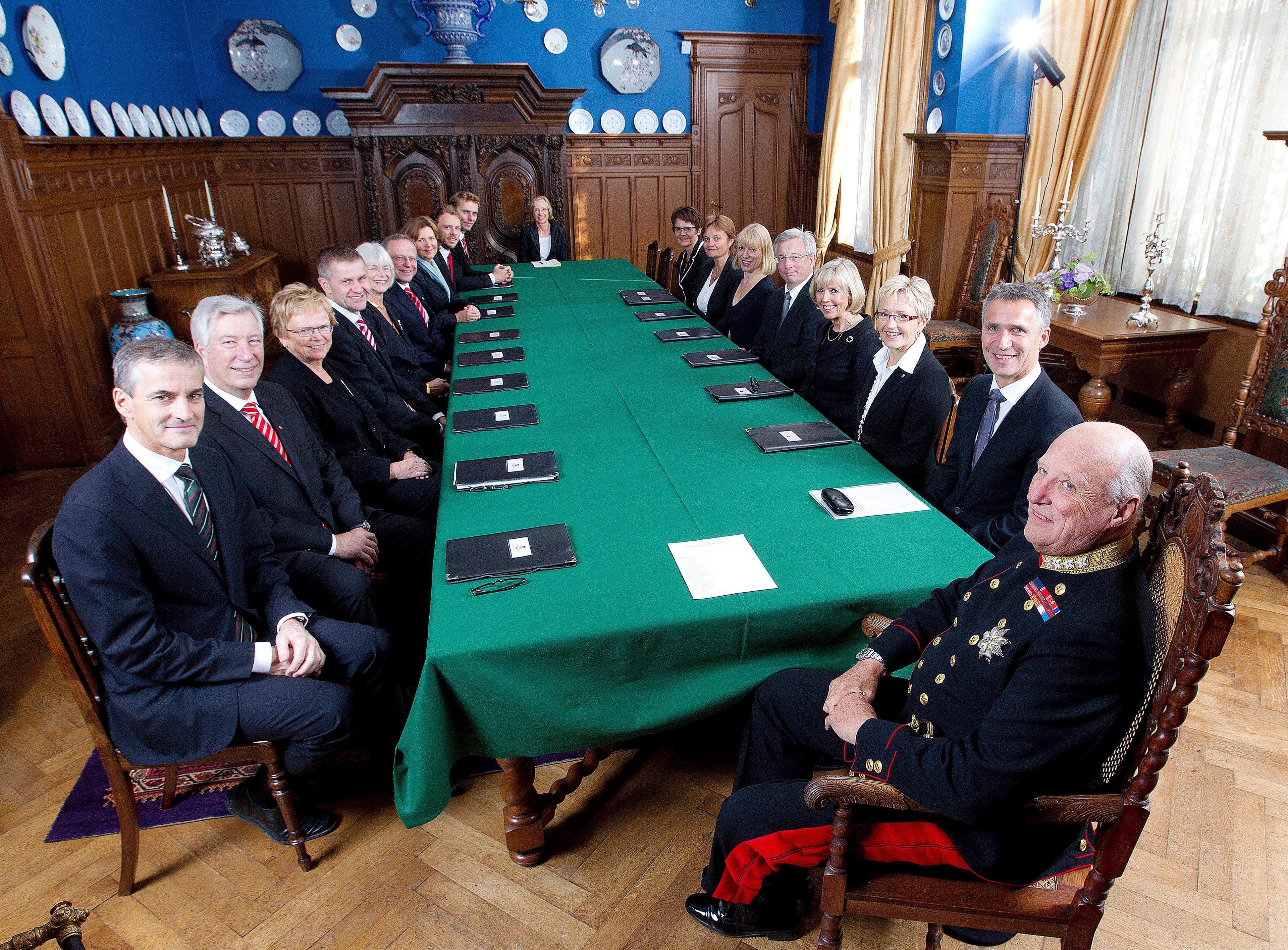 Kongen og regjeringen samlet til statsråd omkring et langt bord med grønn duk. Saksmapper ligger foran alle.