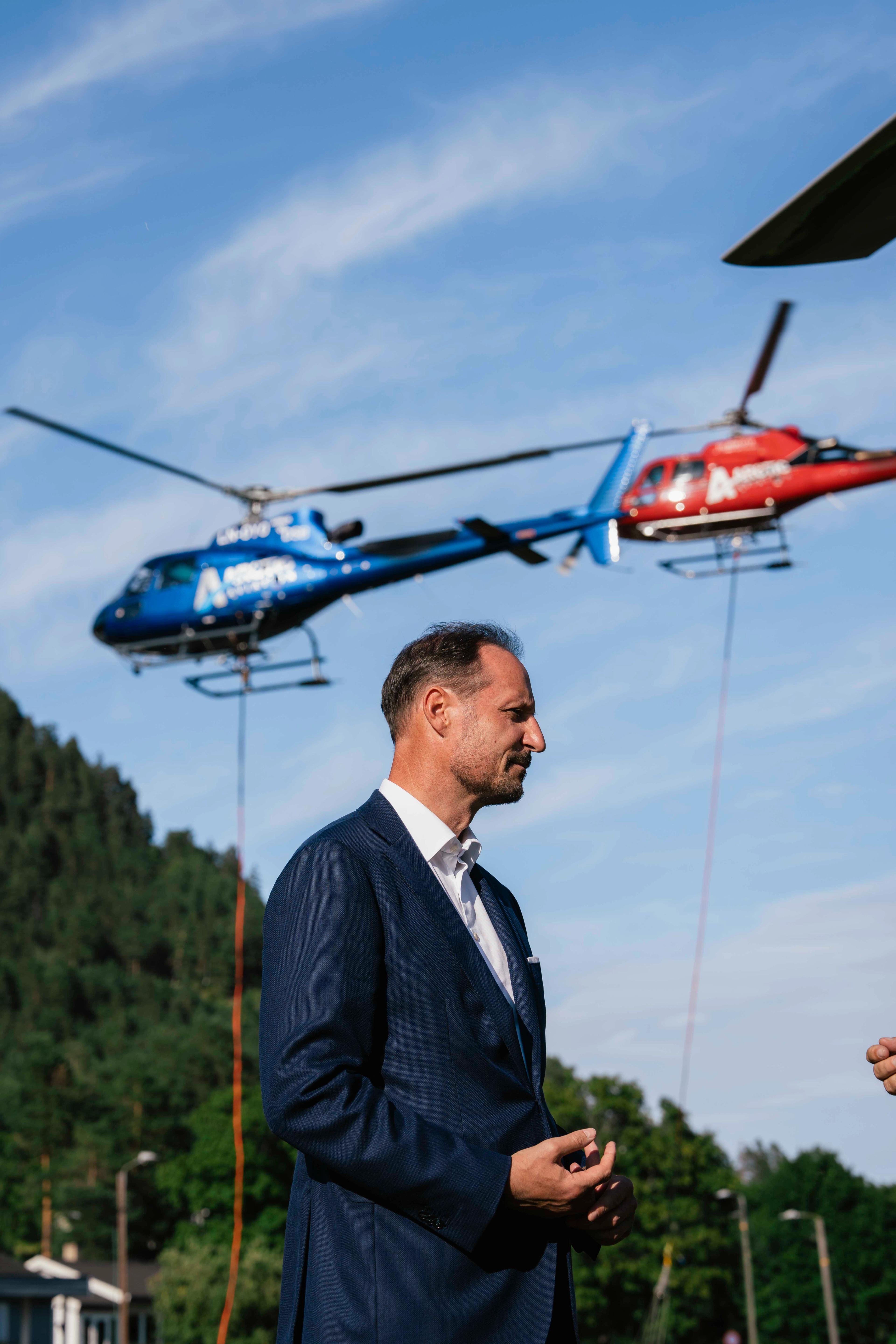 Kronprins Haakon med to helikoptre i luften bak.