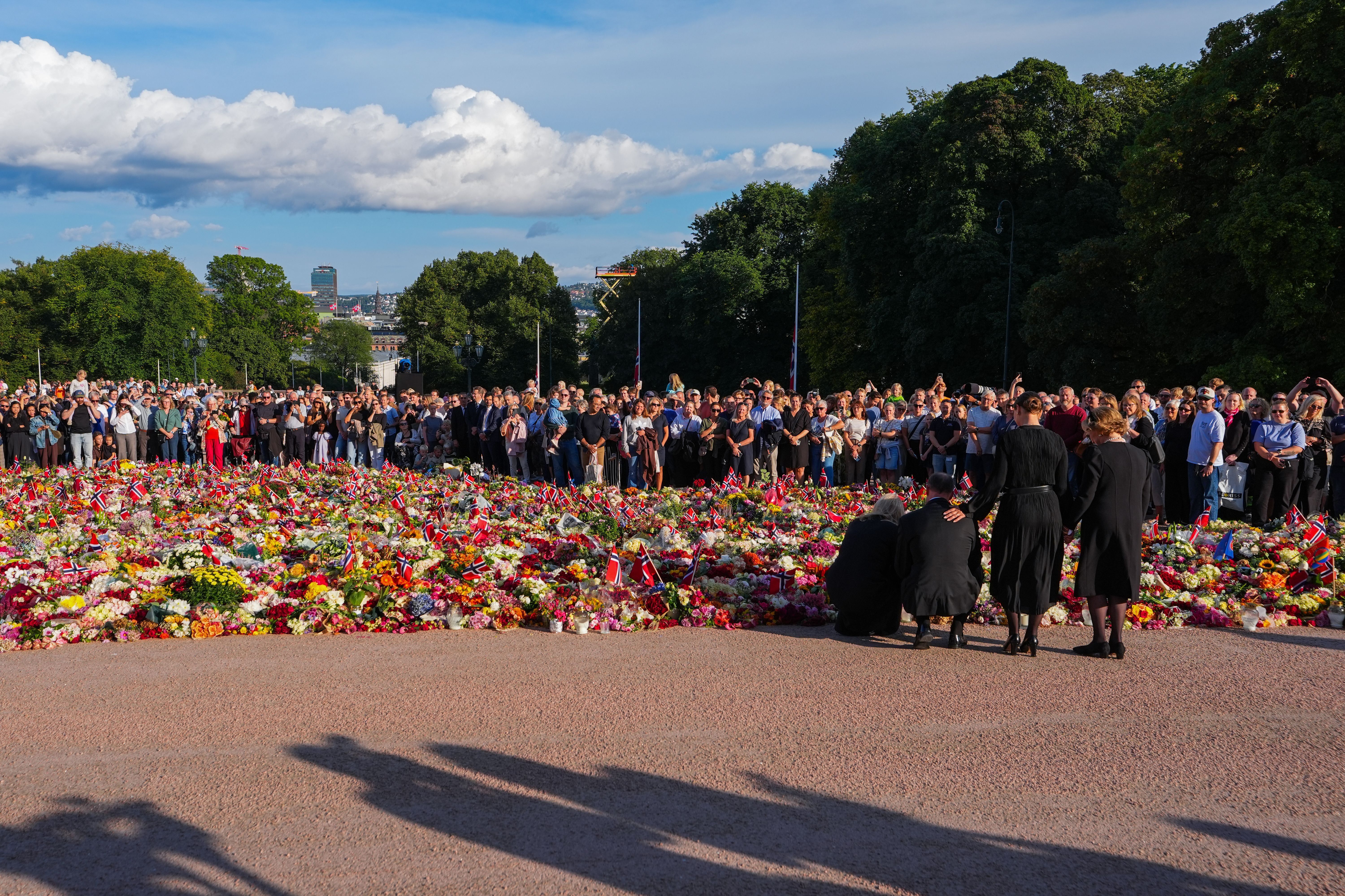 Kong Haakon og Dronning Mette-Marit kneler foran blomsterhavet for å plassere sine roser. Dronning Sonja og Prinsesse Märhta Louise står ved siden av.