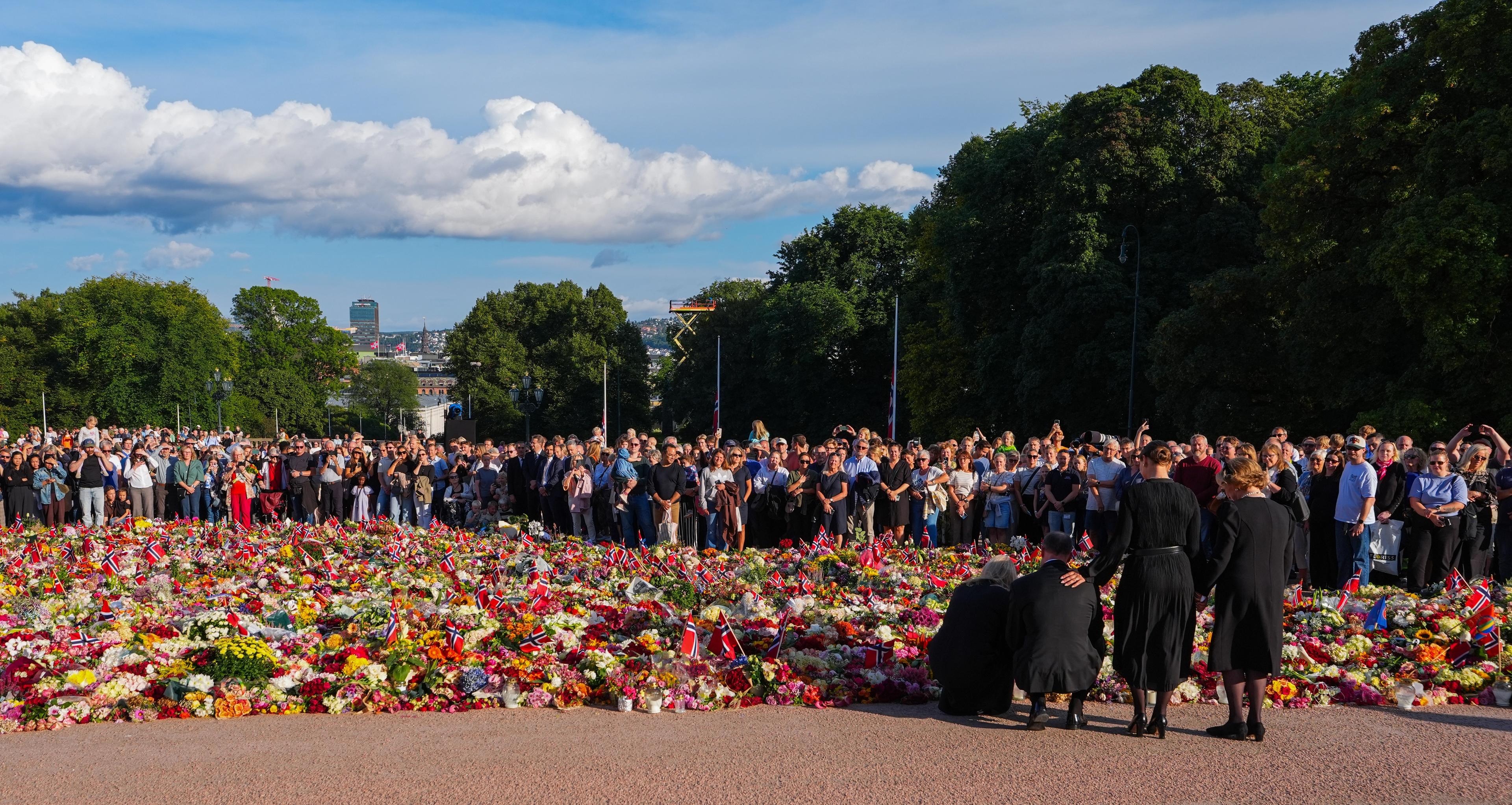 Kong Haakon og Dronning Mette-Marit kneler foran blomsterhavet for å plassere sine roser. Dronning Sonja og Prinsesse Märhta Louise står ved siden av.