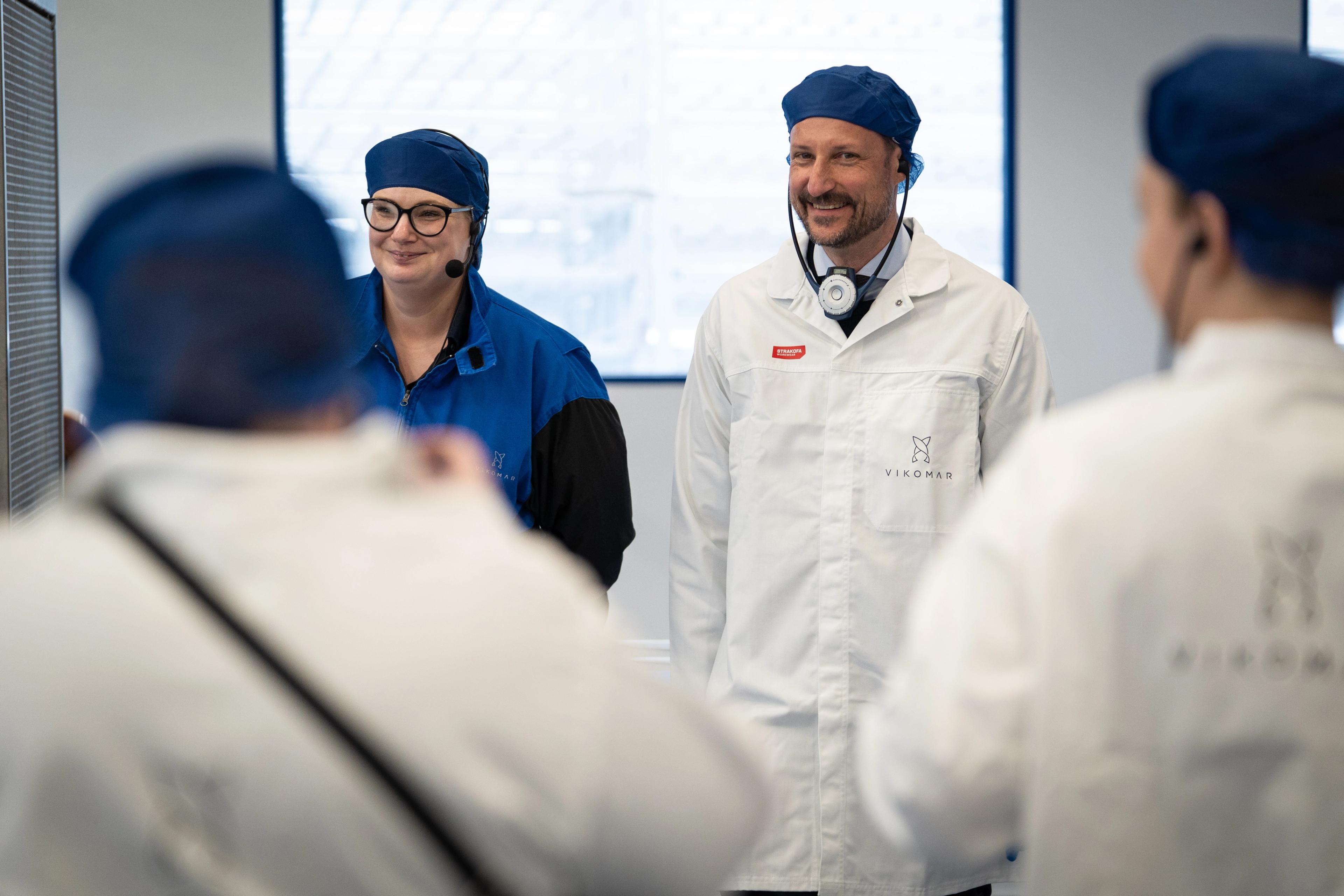 Kronprinsen på omvisning i fabrikken med hvit frakk og blå hettelue.