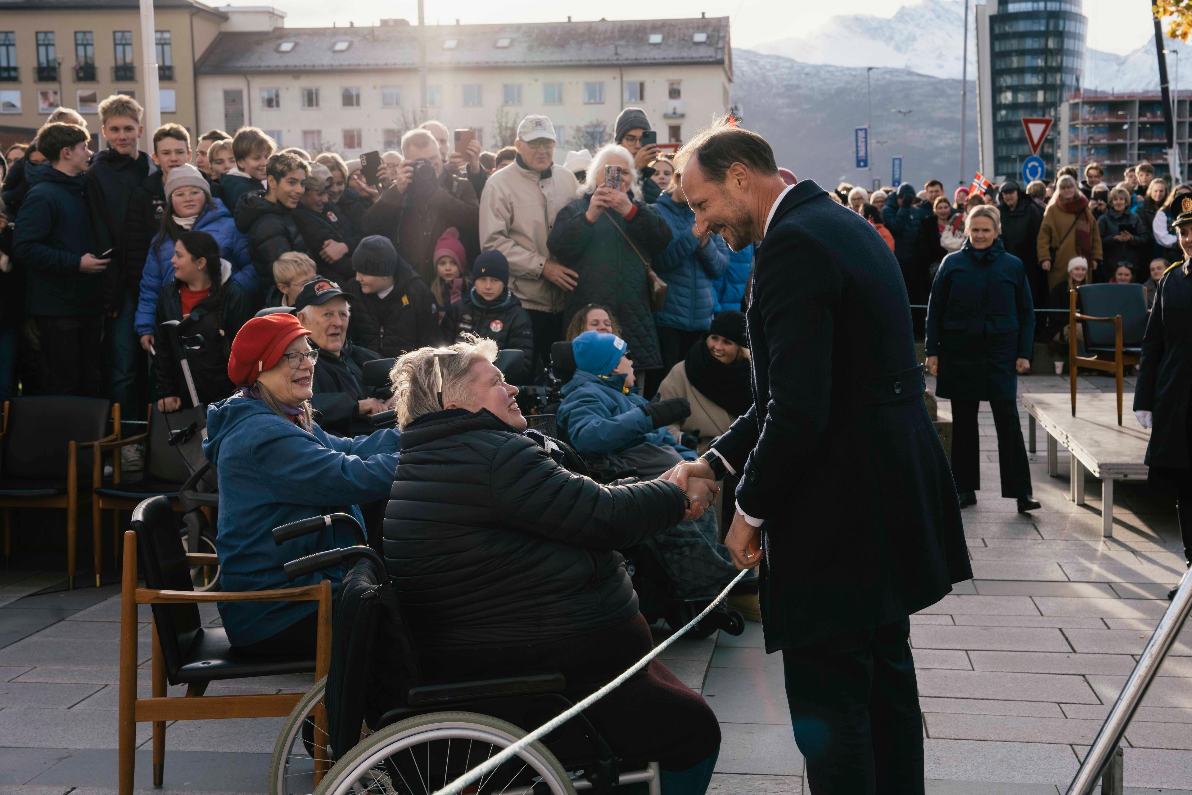 Mennesker er samlet, i første rekke sitter personer i rullestol som hilser på Kongen