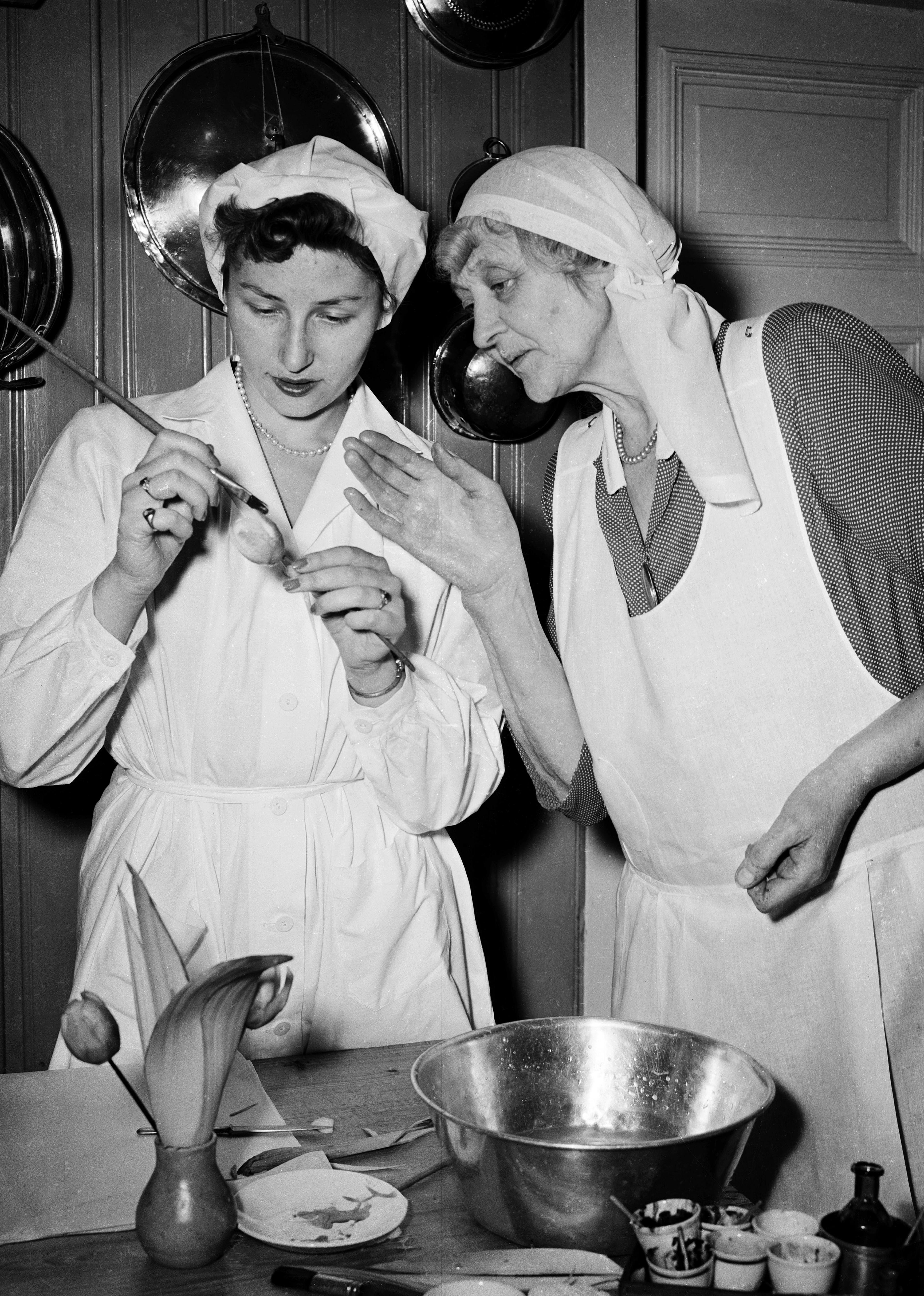 Prinsesse Astrid maler med en håndholdt blomst med tynn pensel. Læreren følger nøye med.