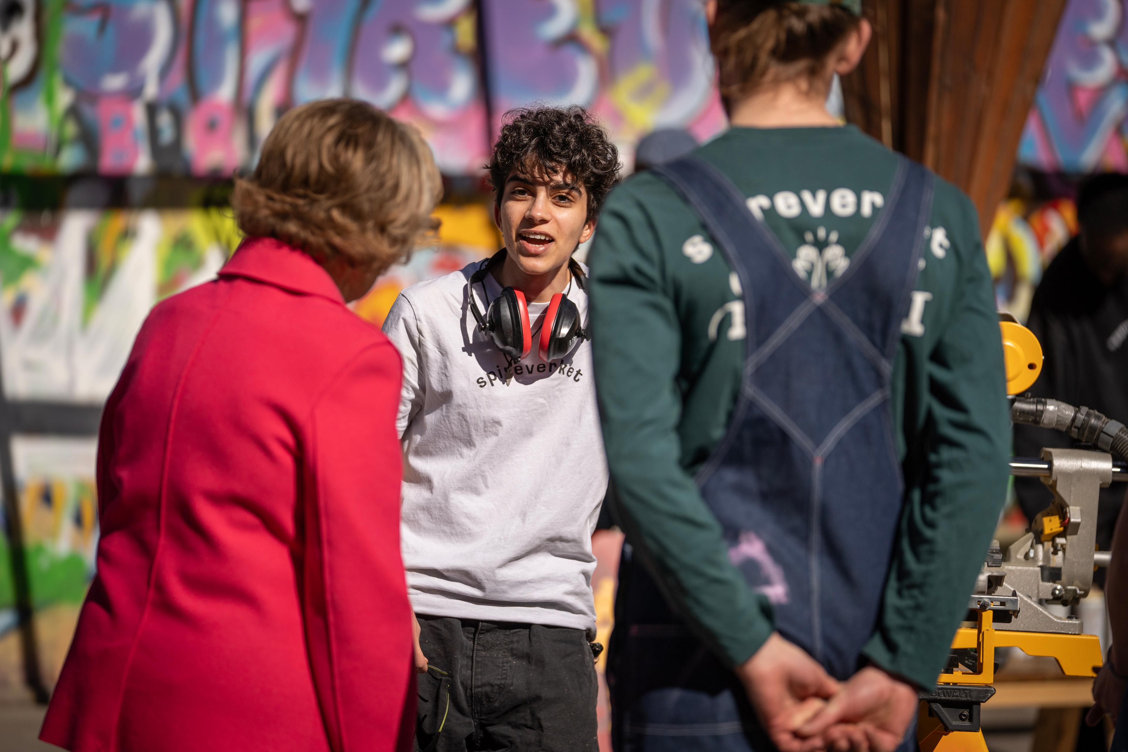 En ung gutt i samtale med Dronning Sonja med hørselsvern rundt halsen.