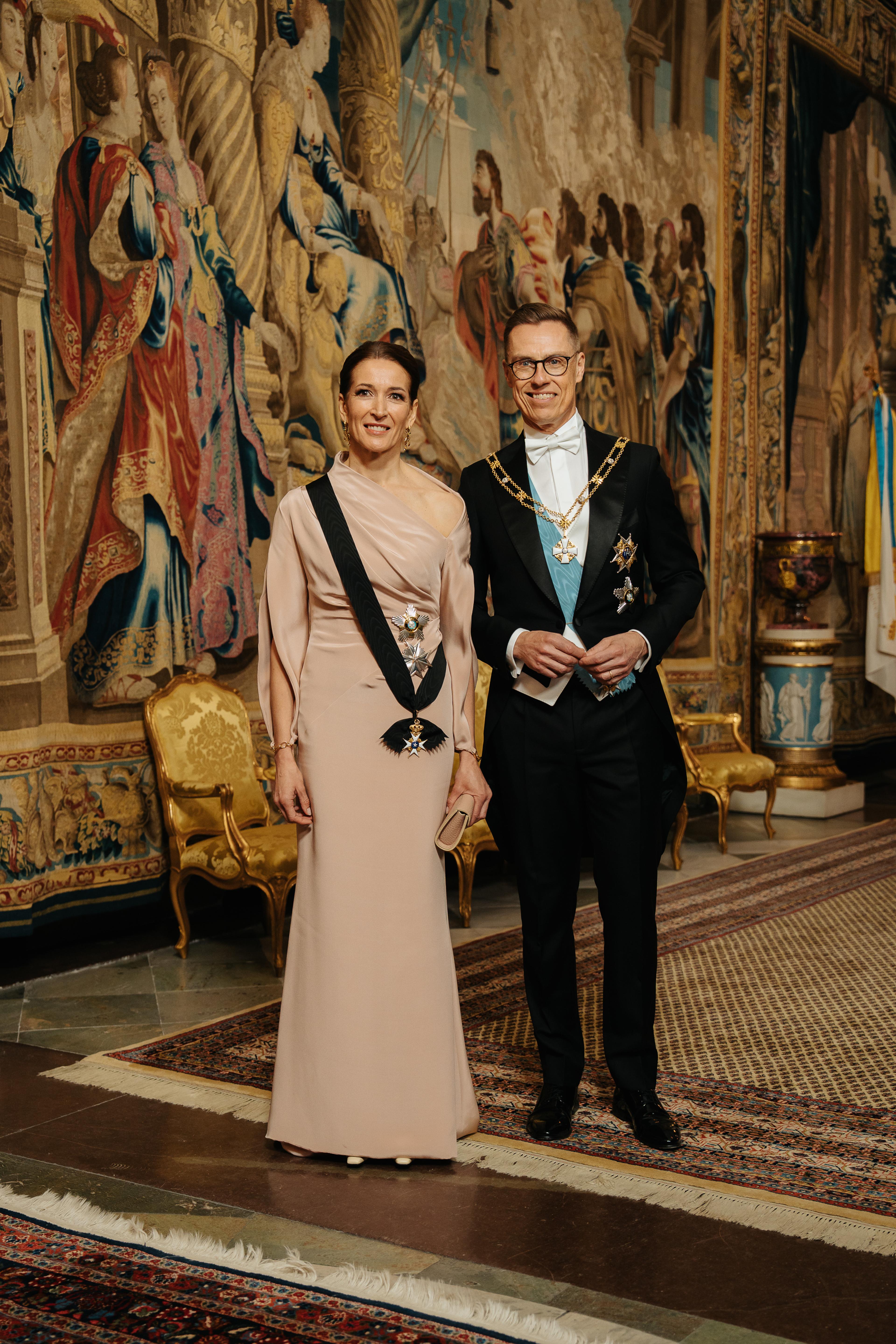 Presidentparet kledd i galla foran et stort veggteppe (gobelin).