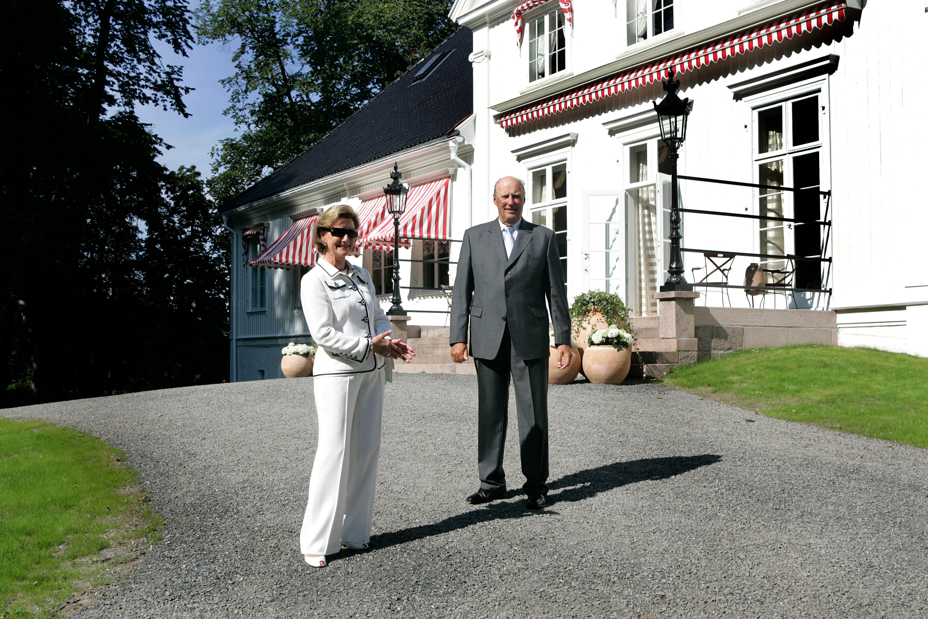 Kongeparet står smilende utenfor Kongsgården en solfylt dag i august