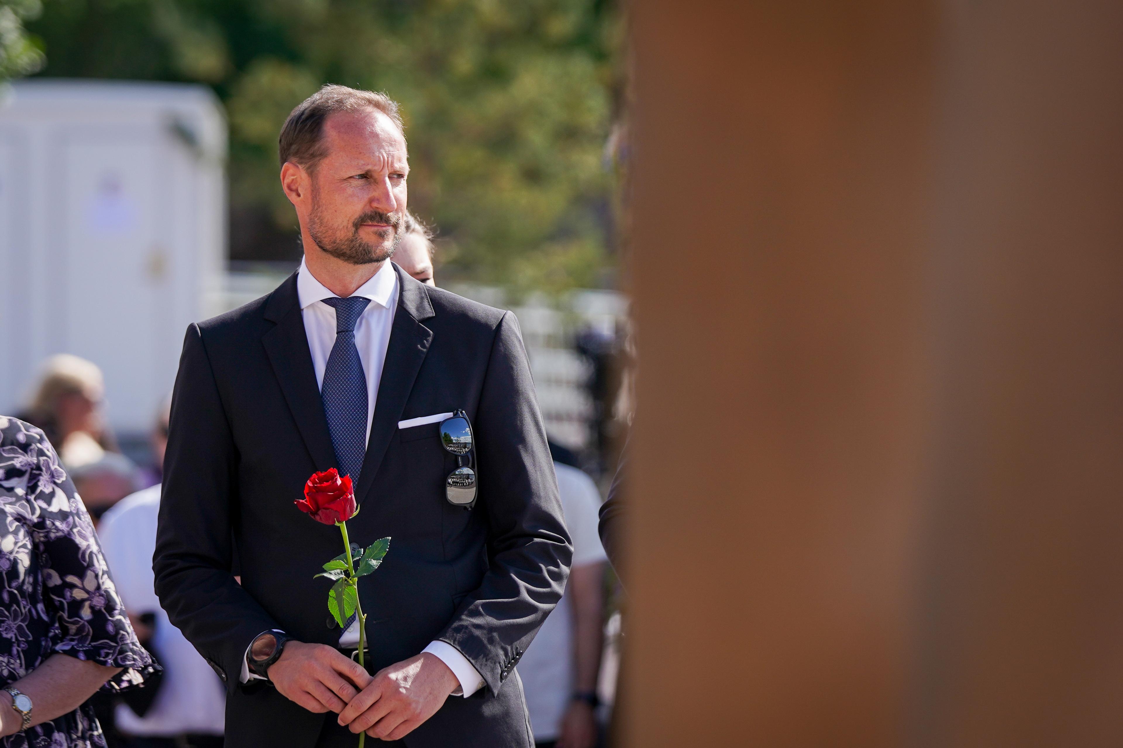 Kronprins Haakon står med en rød rose i hendene og ser mot en av de 77 søylene som markerer hver person som ble drept i terrorangrepene.