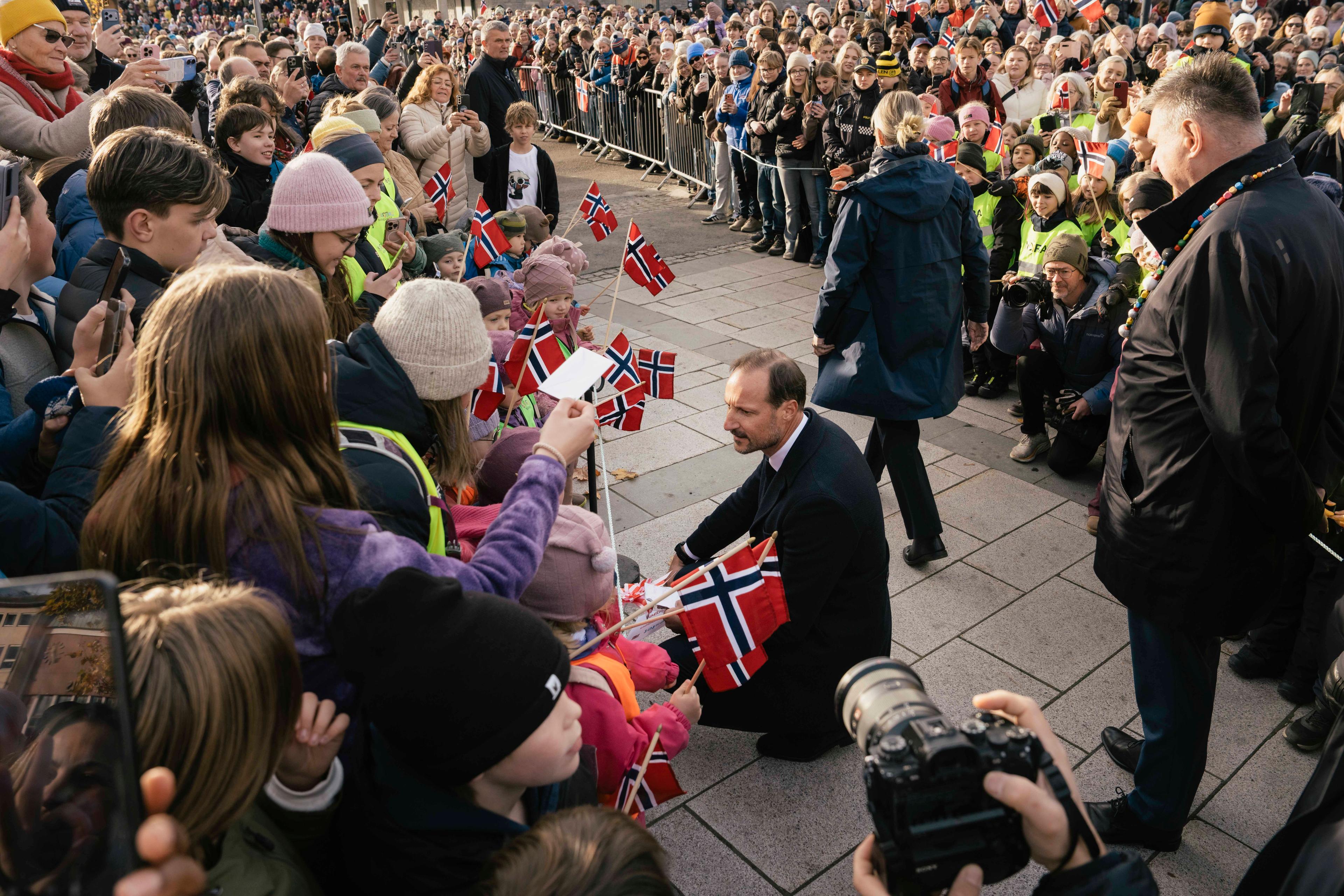 Kongen sitter på huk foran barnehagebarn med norske flagg