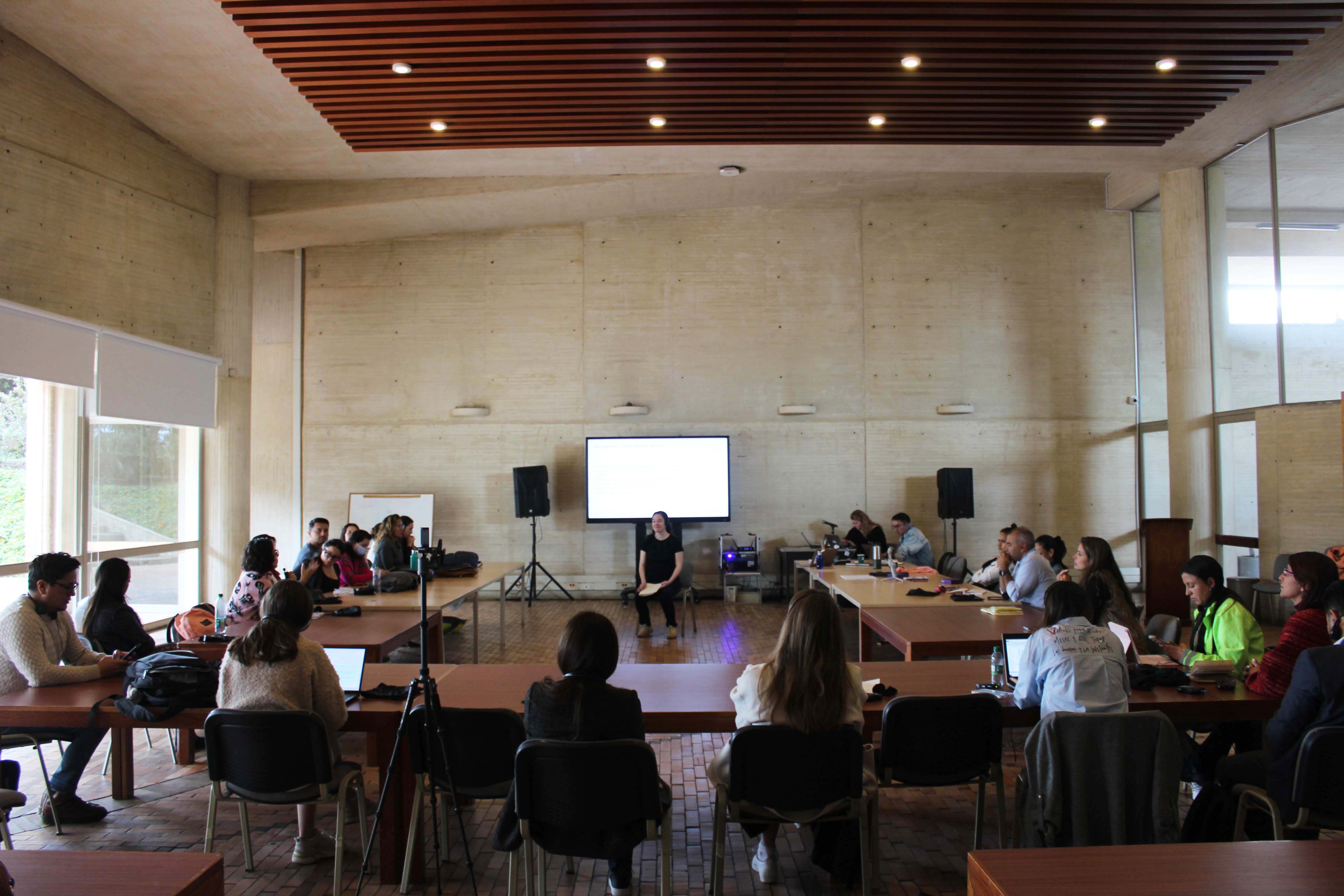A room full of people sitting at desks facing a screen and a speaker.