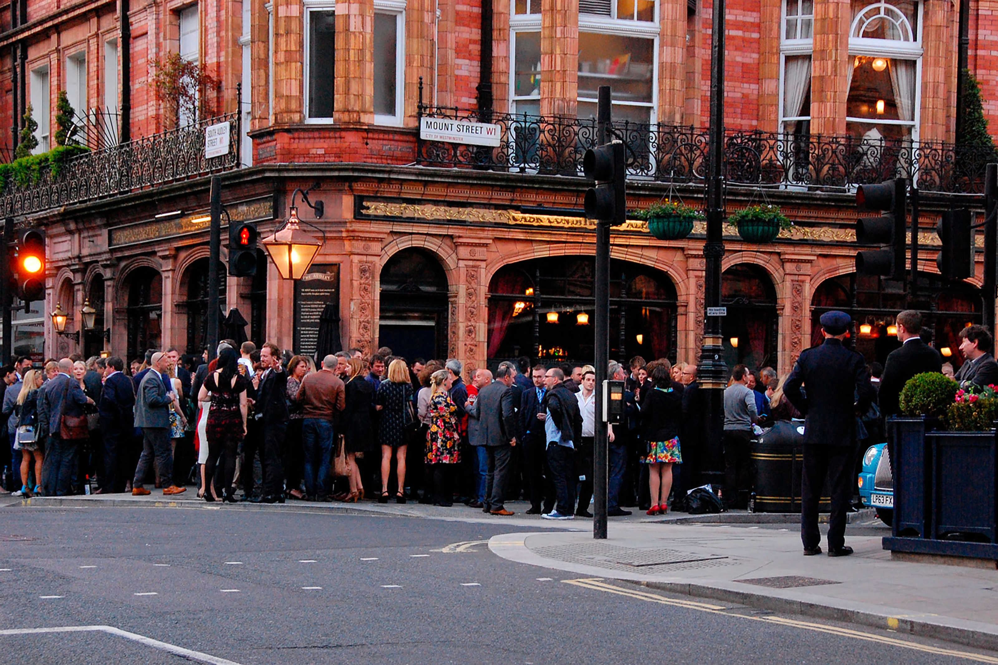 A crowd of people standing outside a pub on a street corner.