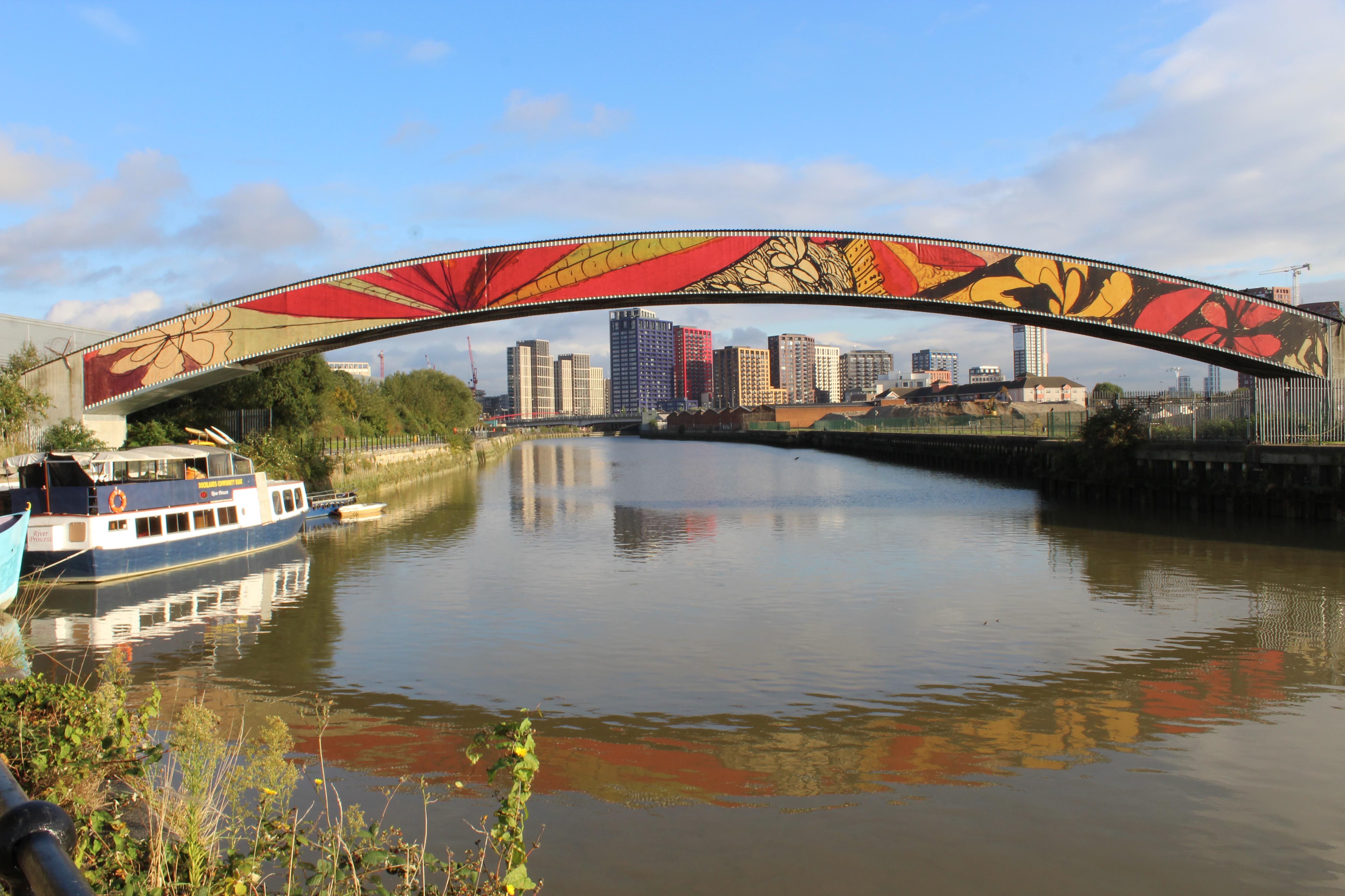 A bridge spanning the Lea River with a colourful  Madge Gill floral pattern along the side of the bridge.