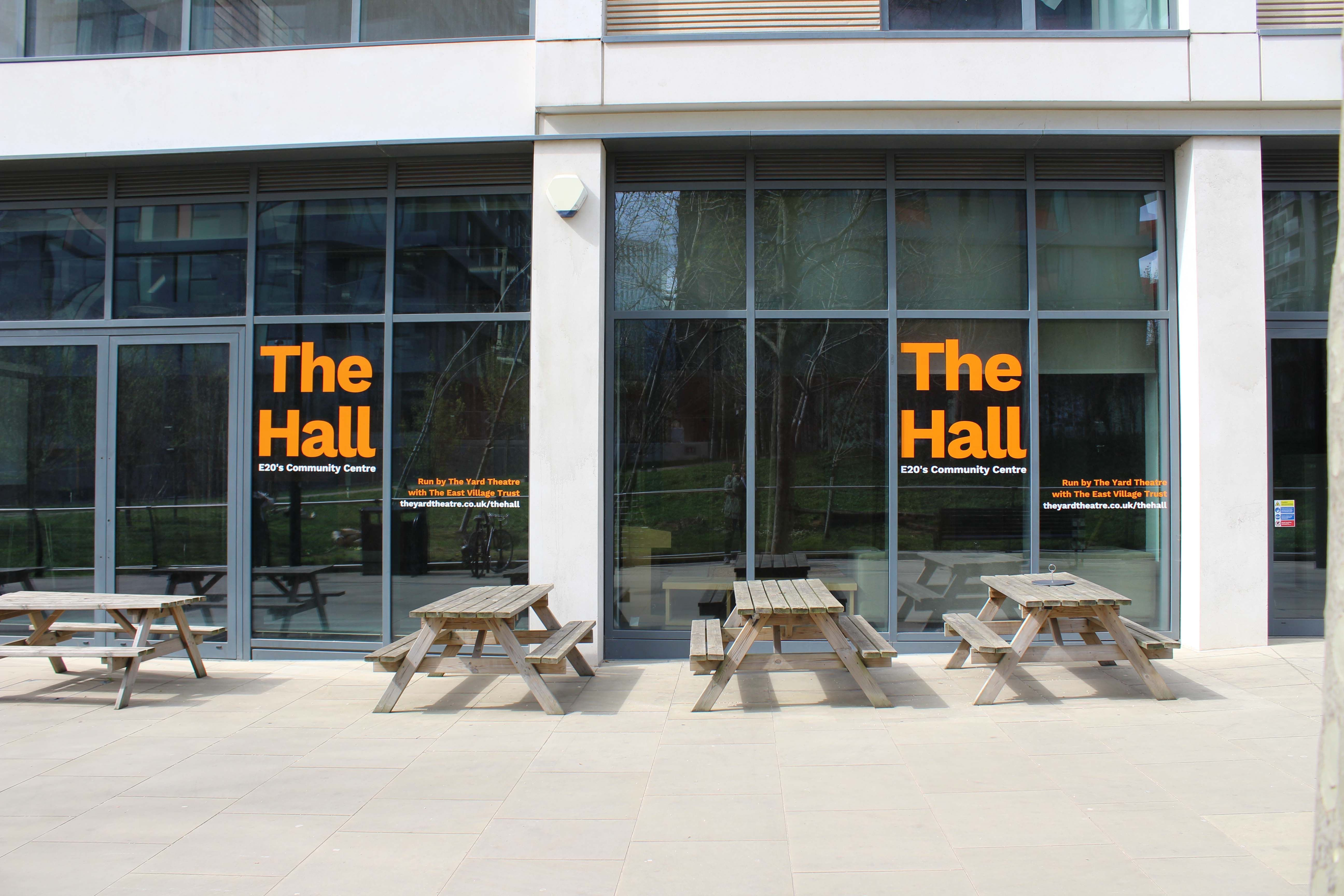 Wooden picnic tables outside a community space with large double height windows.