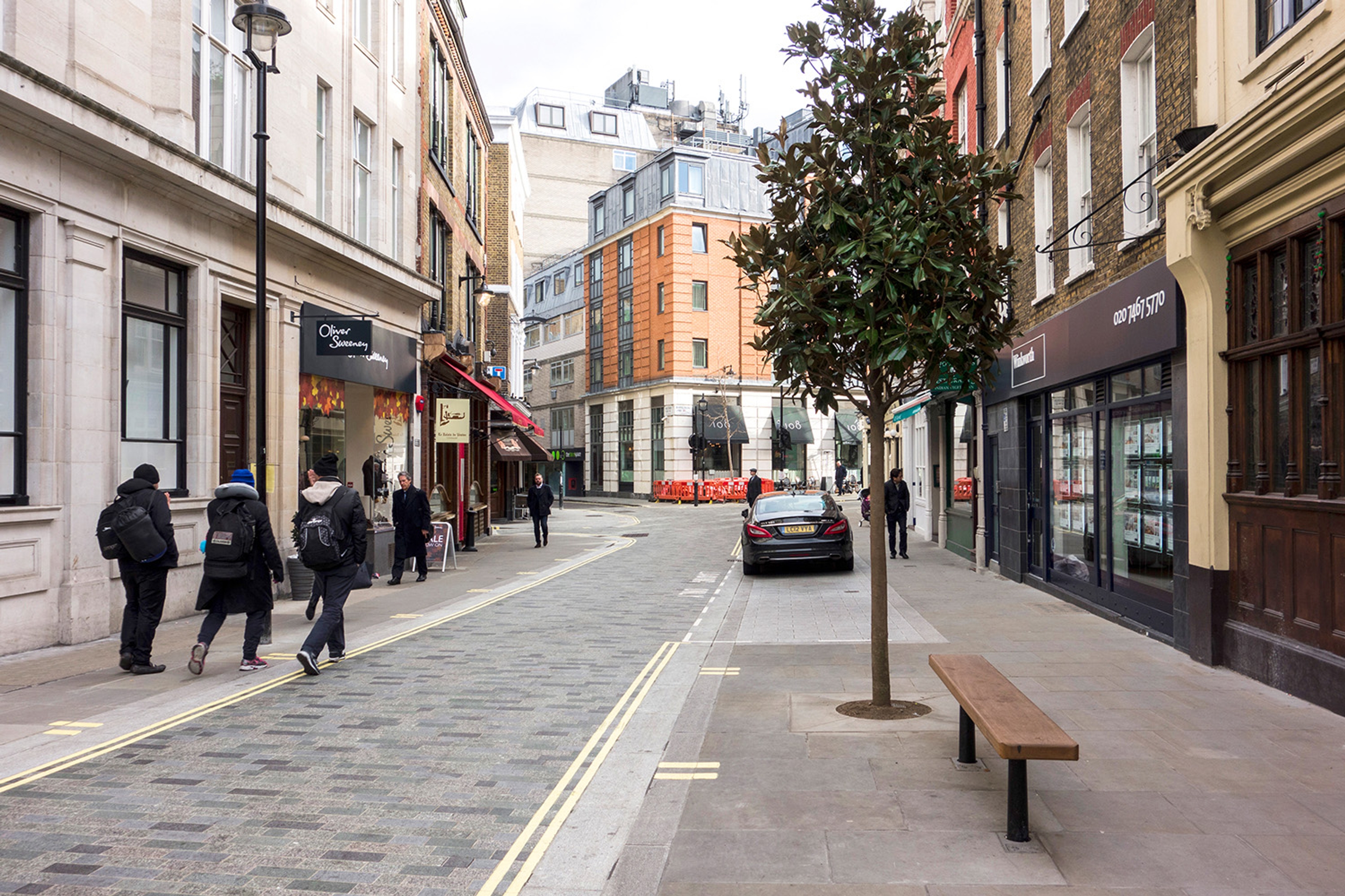 View of the completed Marylebone Lane design with a bench and tree and pedestrians walking along the pavement.