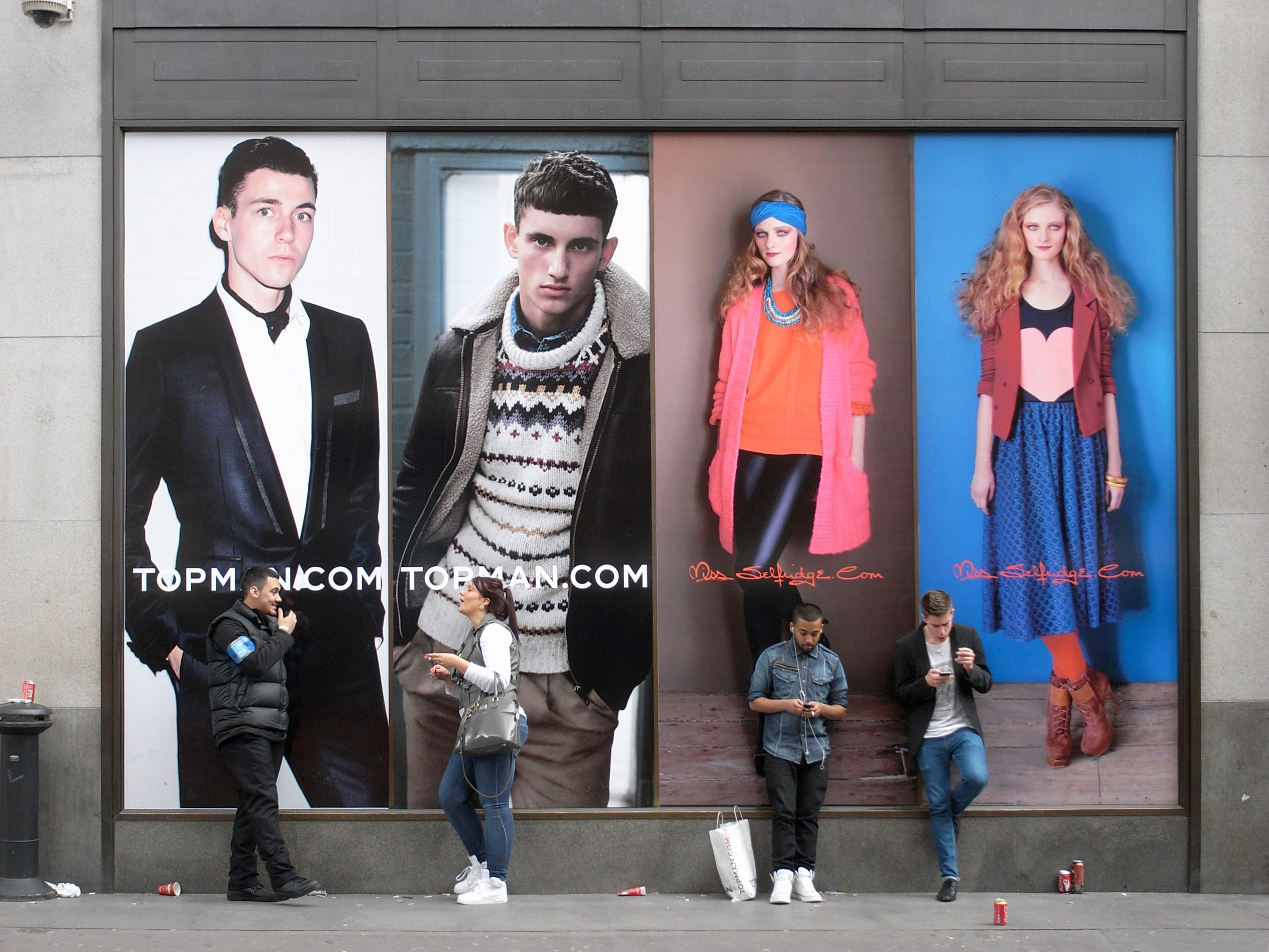 Four people leaning against a billboard for Topman and Miss Selfridges.