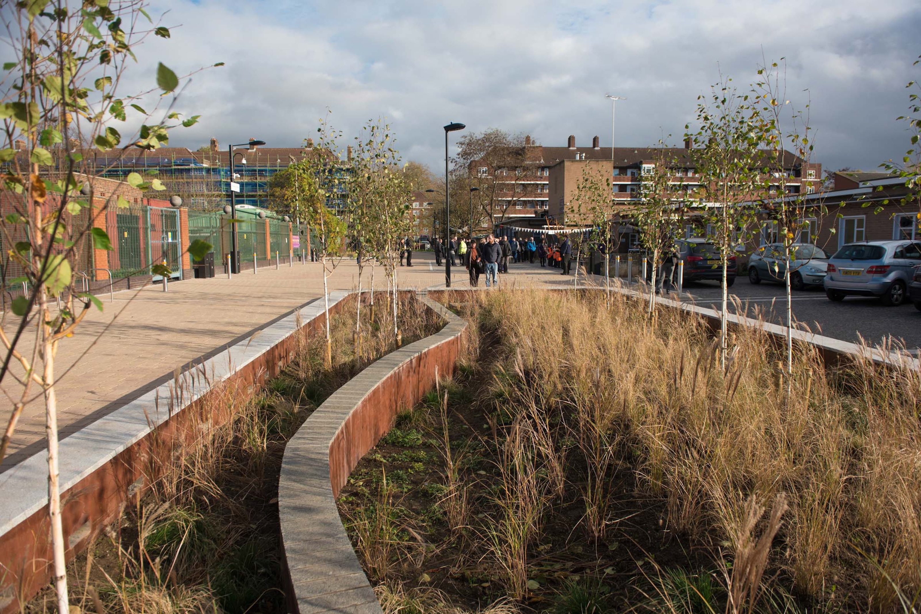 A raised path through a area of planting connecting to a public space.
