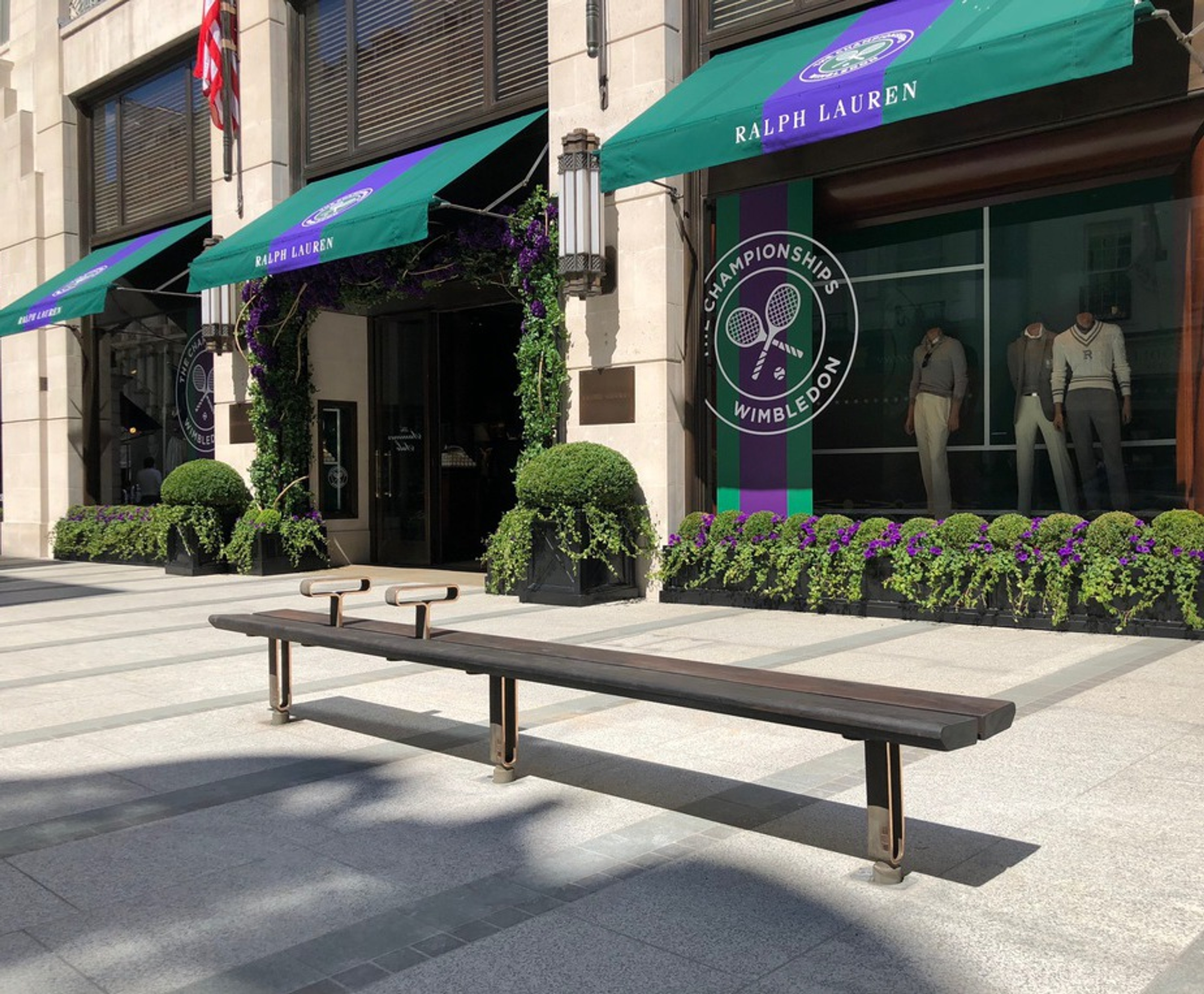A long wooden bench on a pedestrianised street in front of a Ralph Lauren shop.