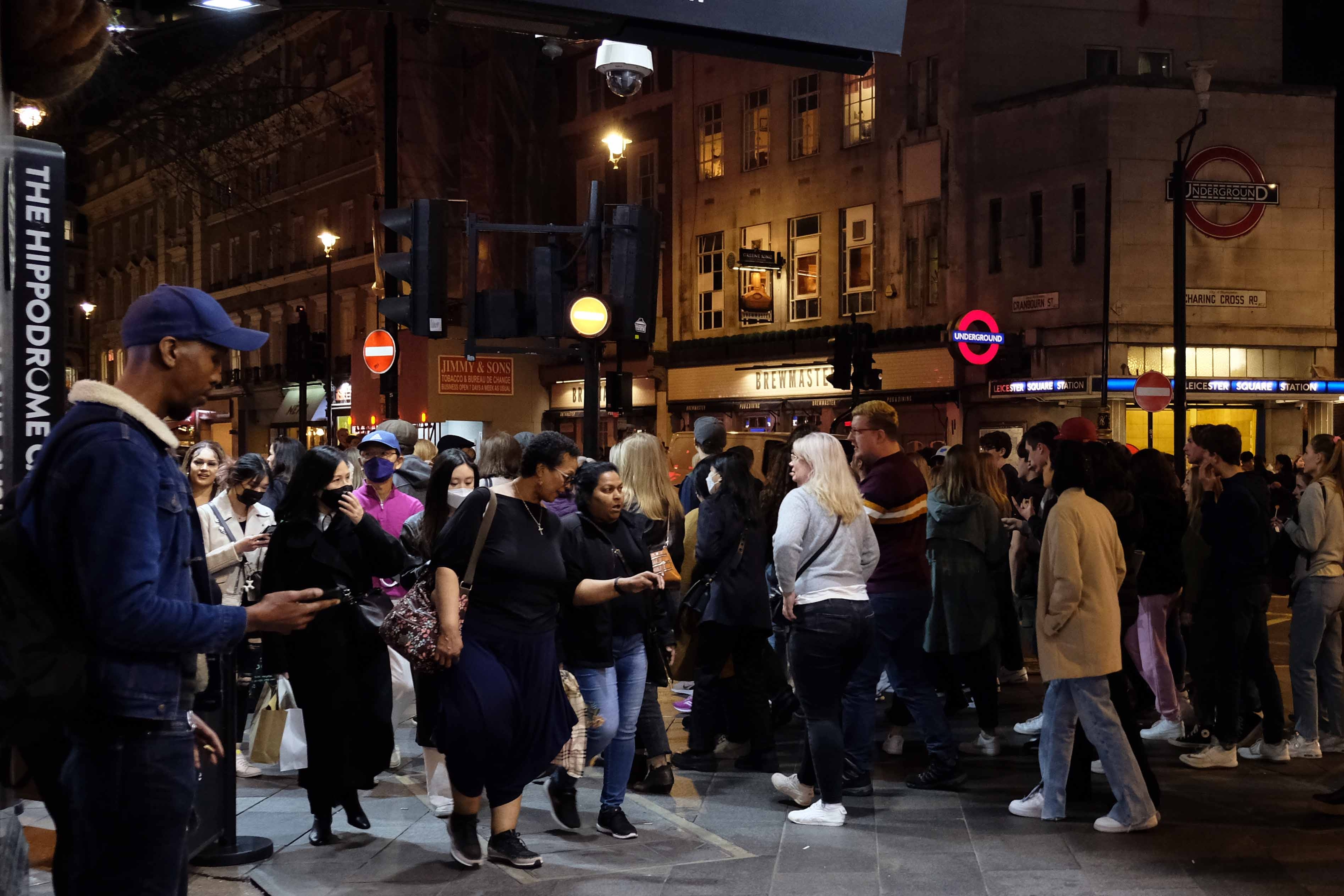 A crowded pavement at night outside Leicester Square Station.