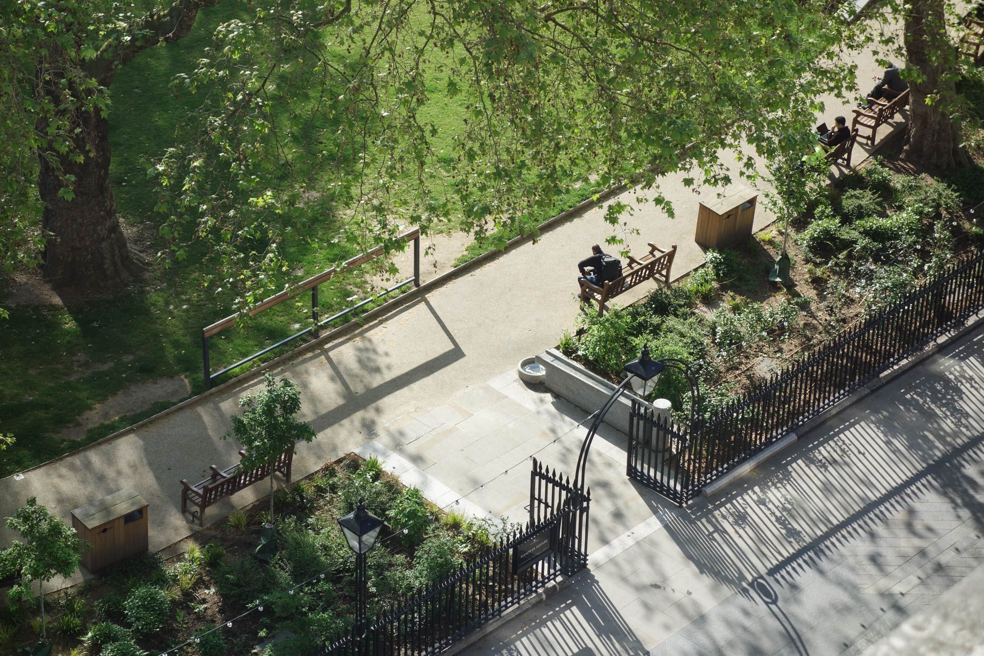 Photograph of the edge of Hanover Square taken from above with grass, bushes and people sitting on benches.