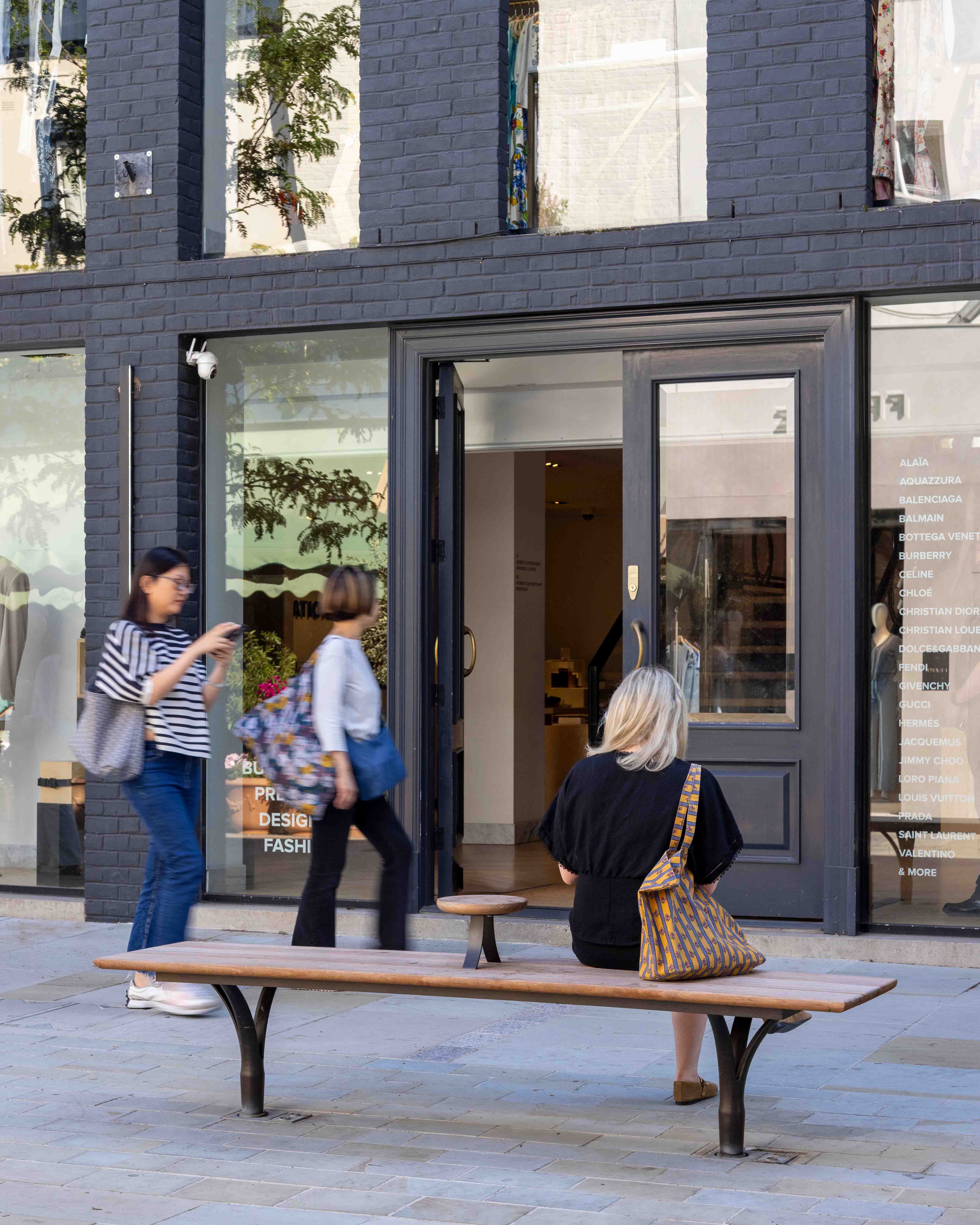 Pedestrians walking past woman sitting on bench facing away from the camera.