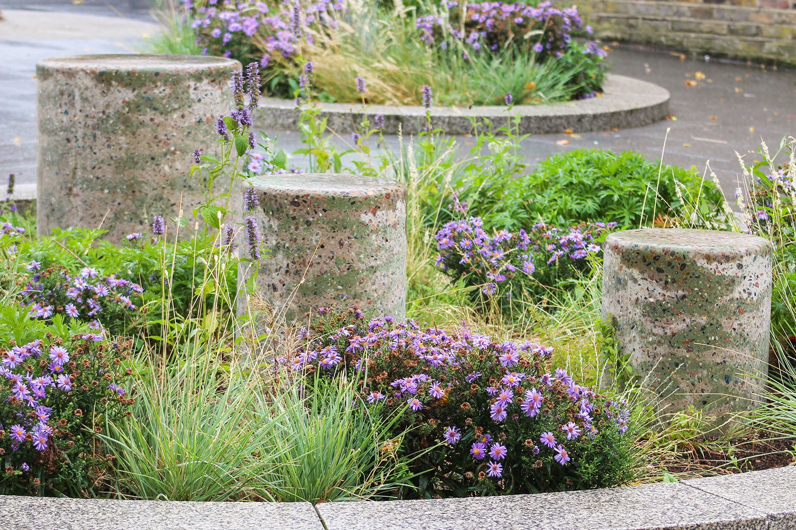 Three stone cylinders surrounded by grass bushes and flowers.