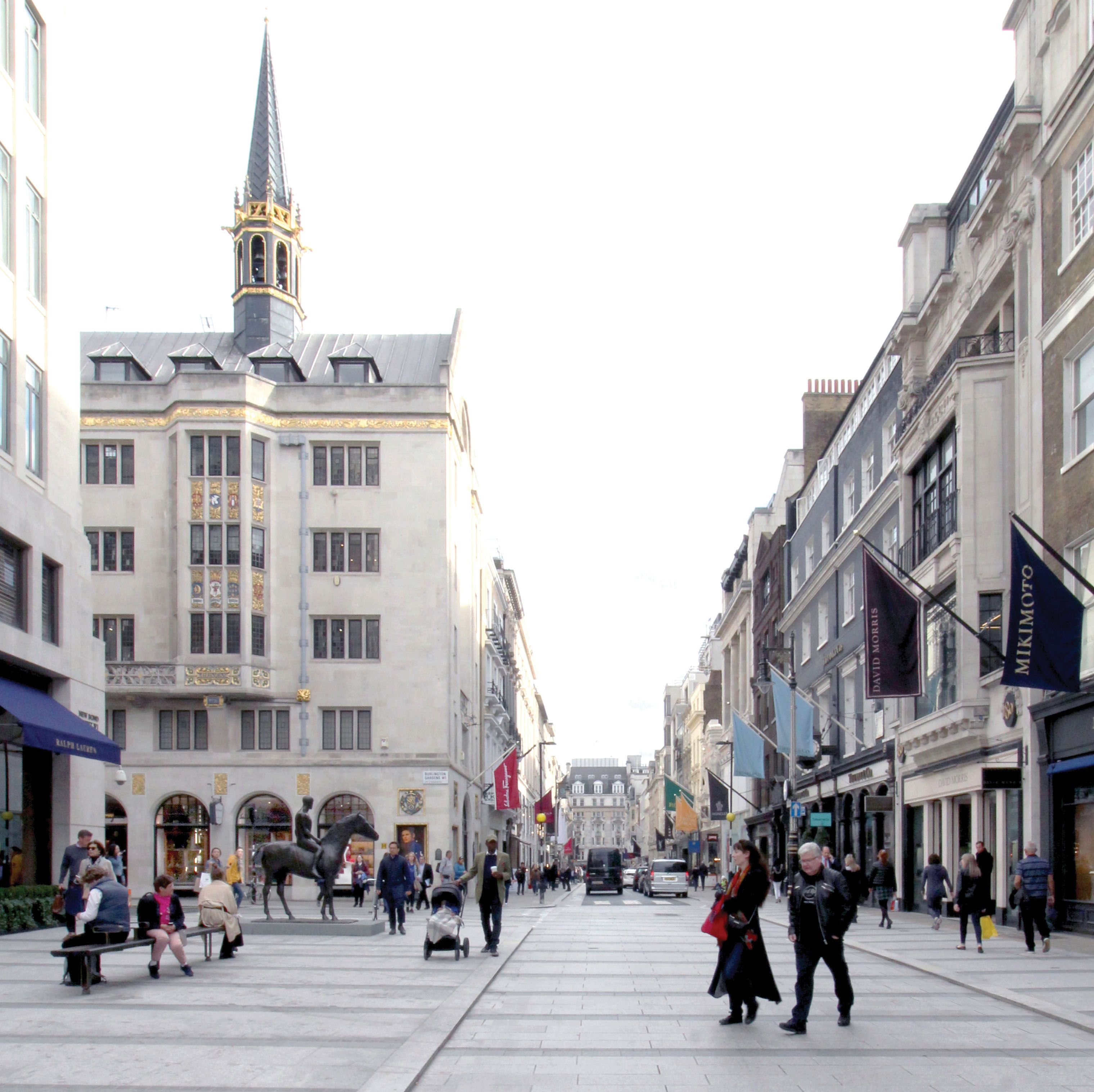 Pedestrianised road showing shop fronts, a statue and people walking.