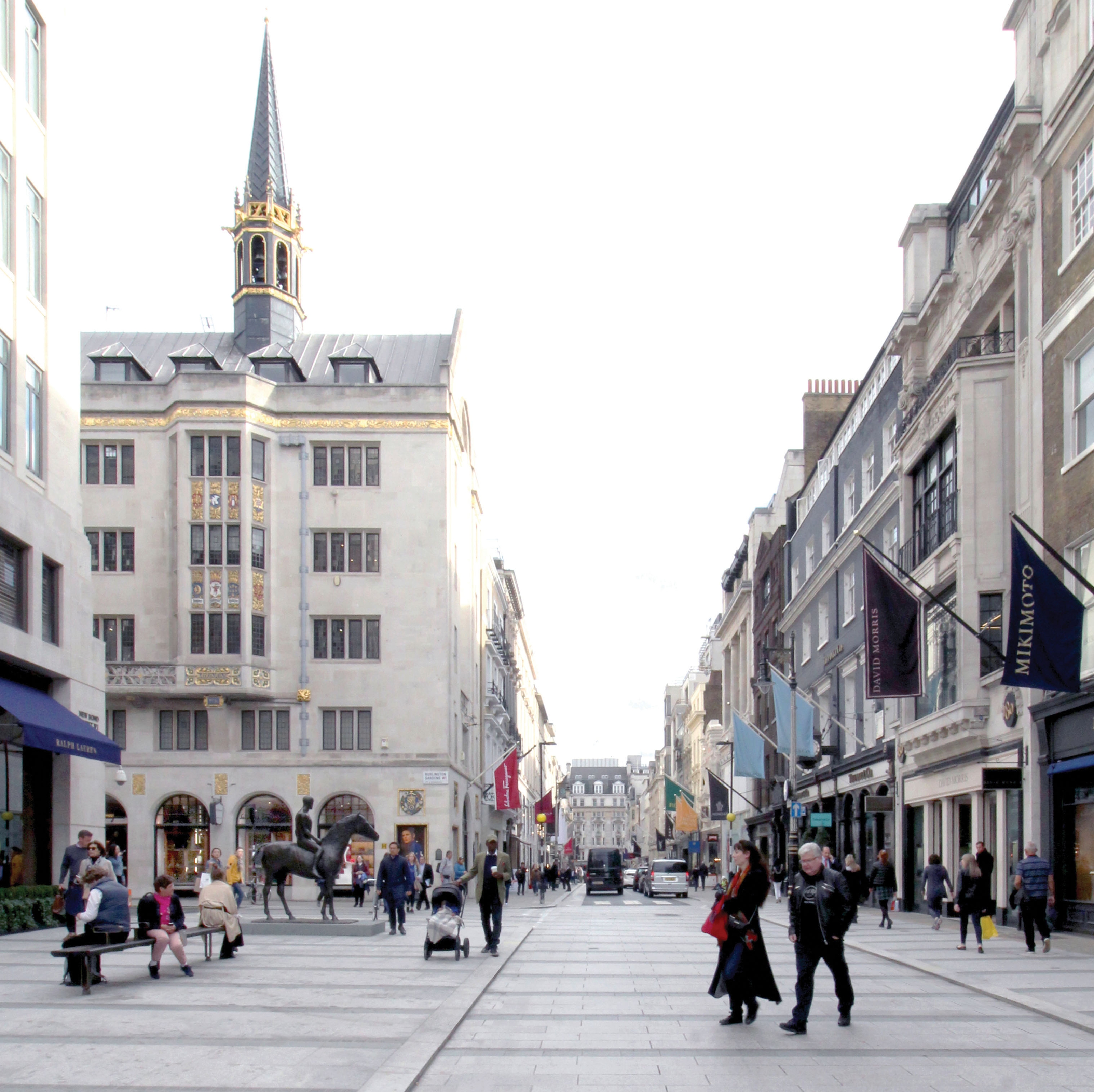 Pedestrianised road showing shop fronts, a statue and people walking.