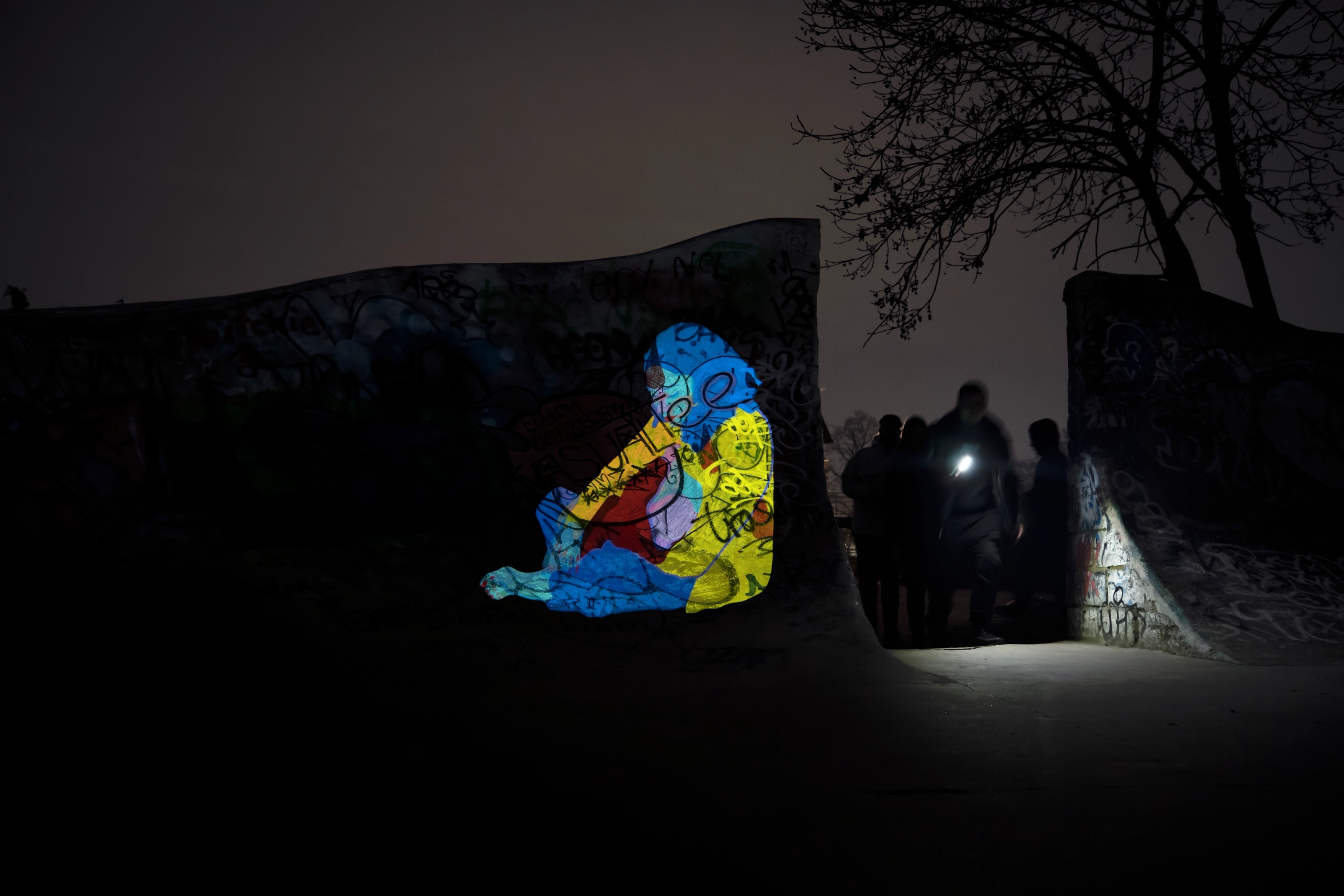 A light projection shows a seated figure as a group of people walk past with a torch.