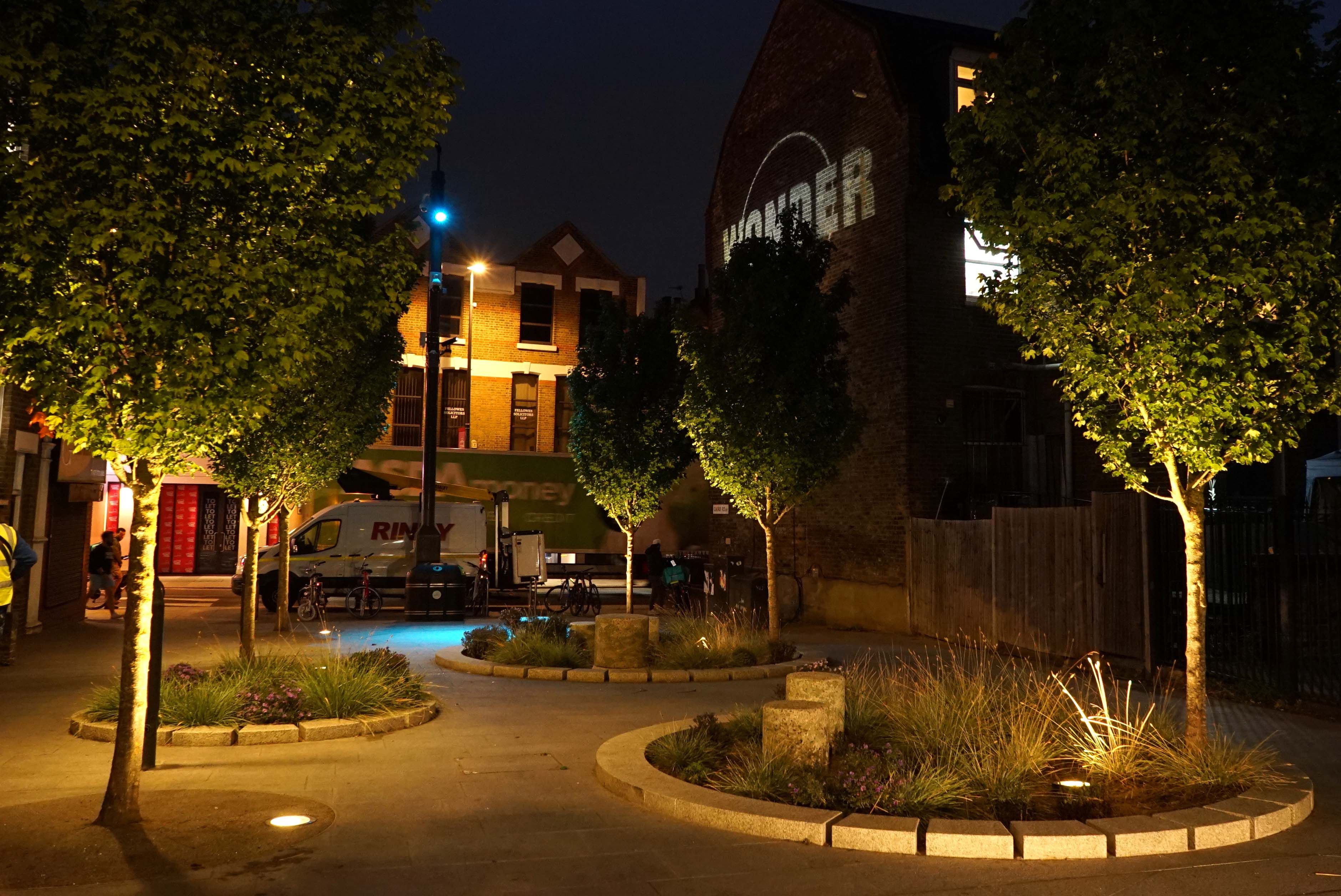 Three planting beds lit by street lamps at night with trees between.