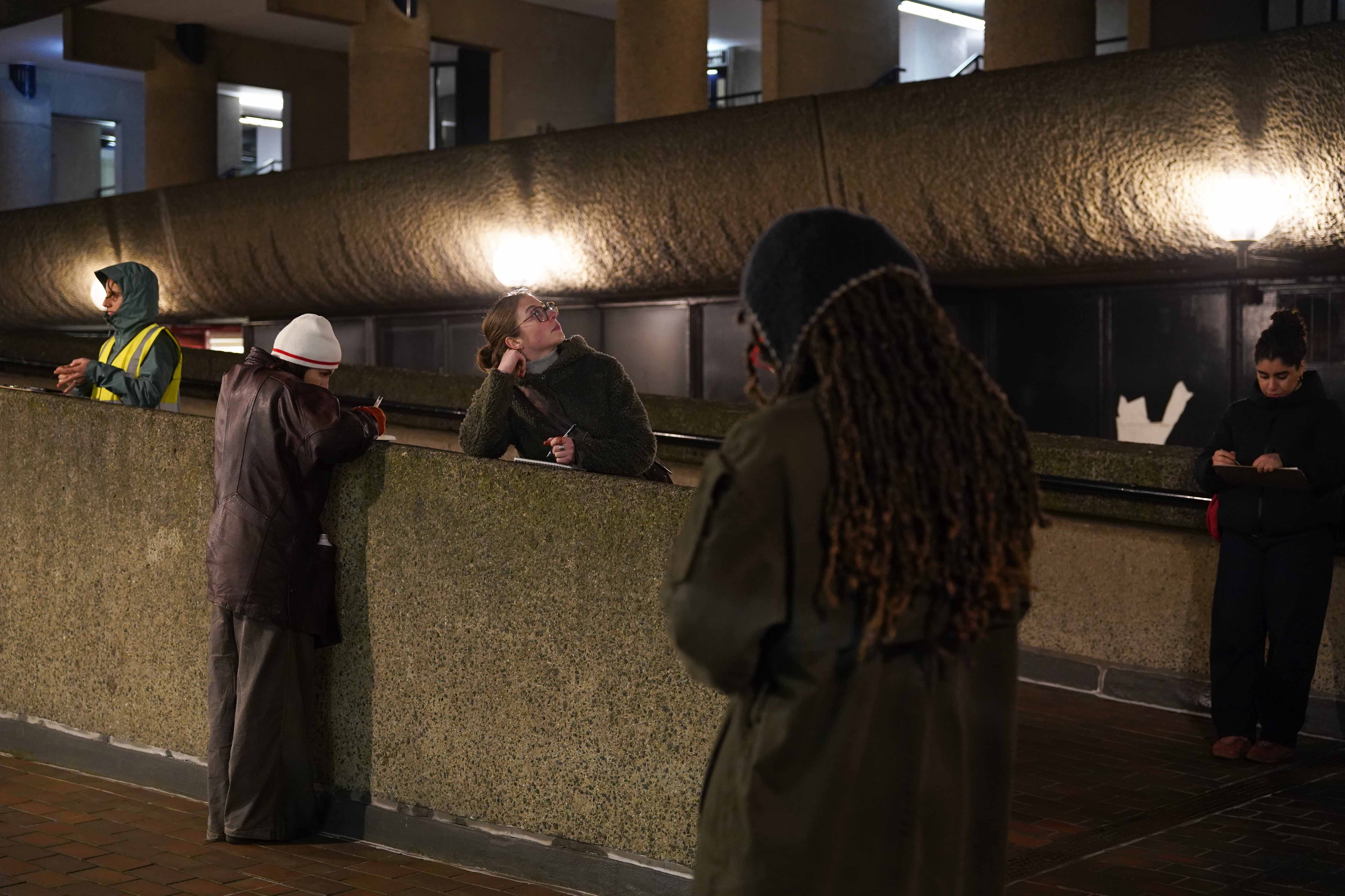 A group of people standing and writing in a concrete elevated walkway at night.