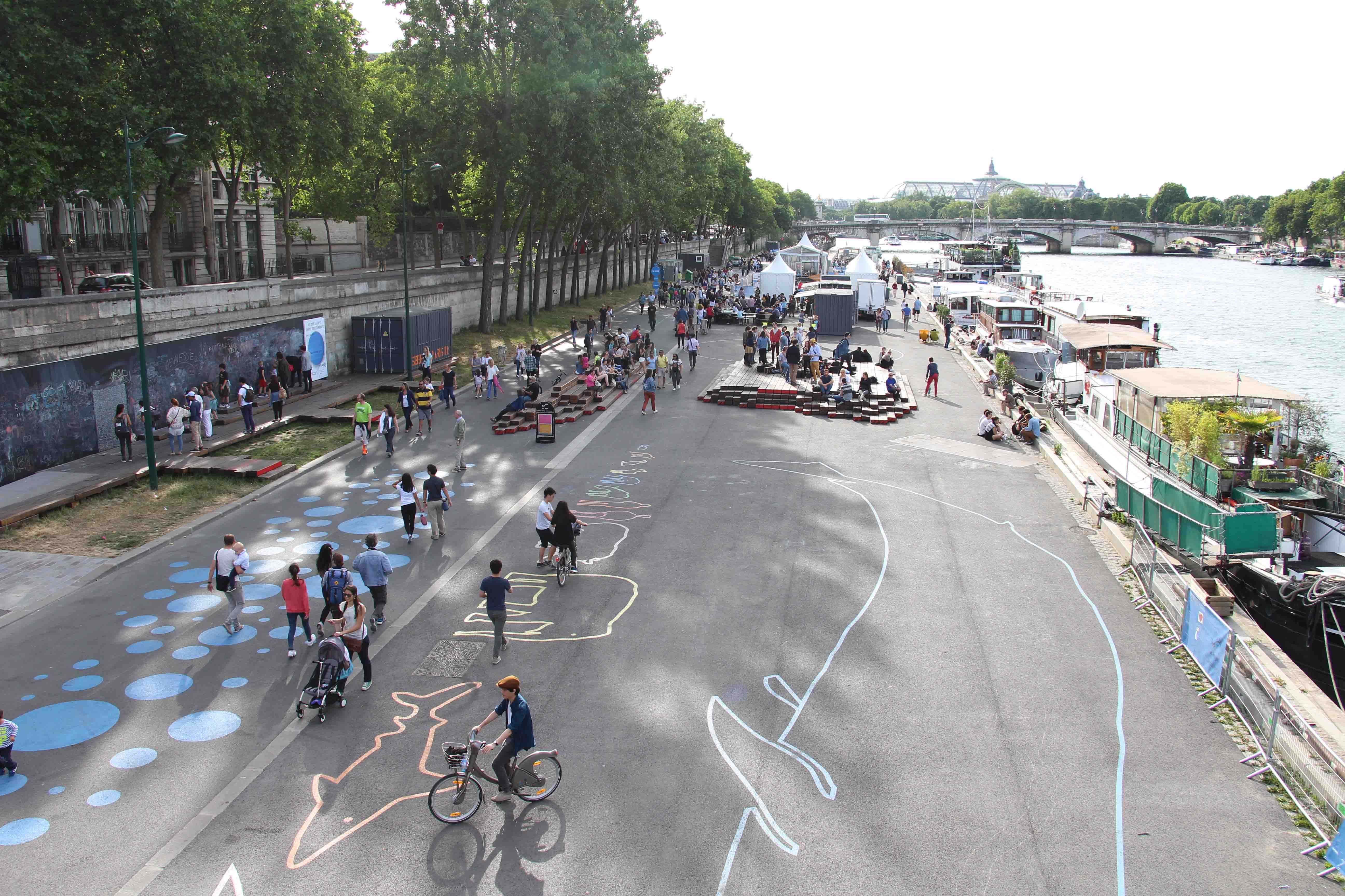 The car-free left bank of the Seine River in Paris with children playing and riding bicycles on the street with play installations and painted patterns and shapes on the carriageway. 