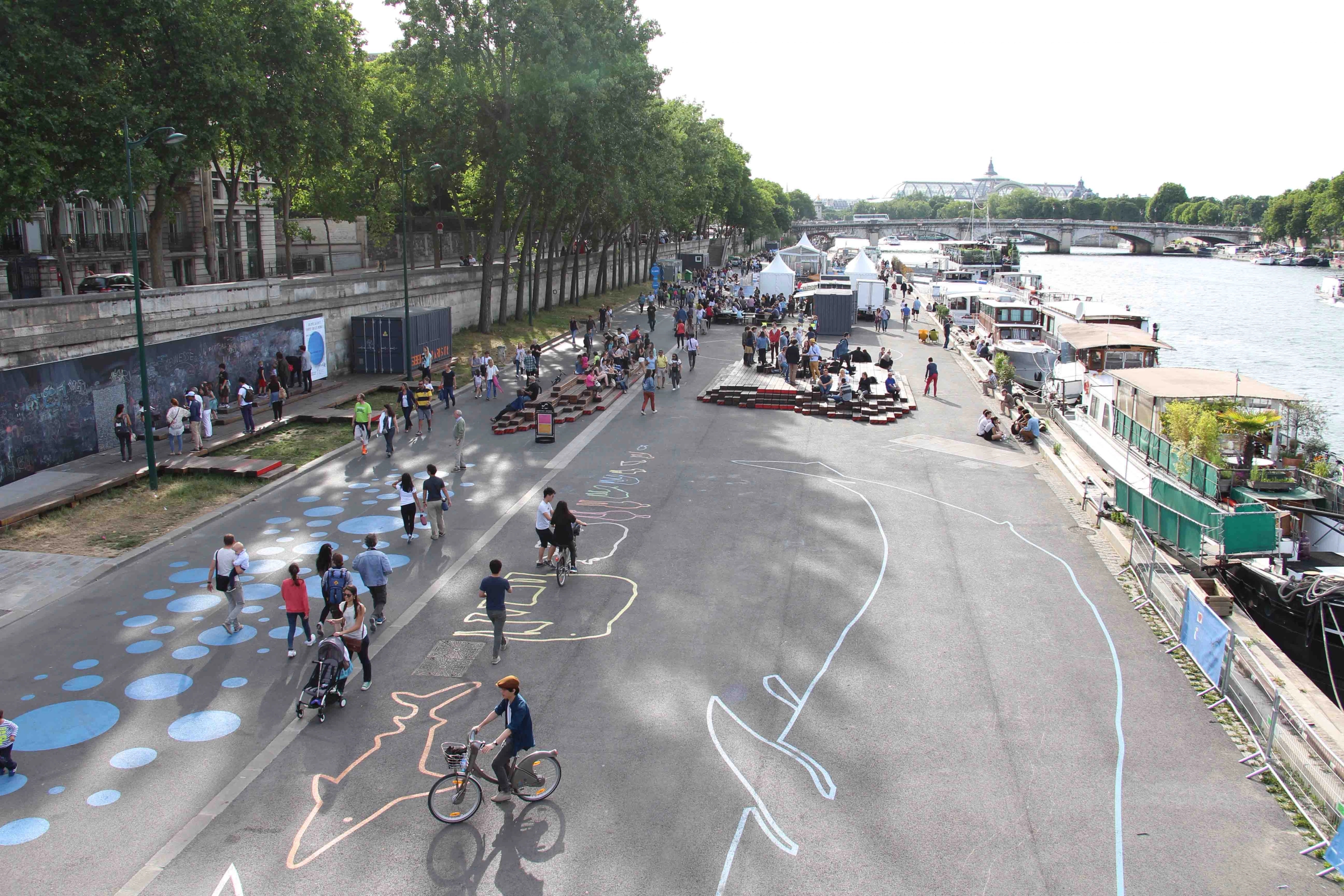 The car-free left bank of the Seine River in Paris with children playing and riding bicycles on the street with play installations and painted patterns and shapes on the carriageway.