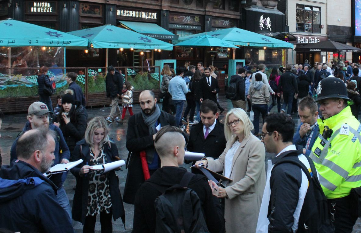 People standing in a street with clipboards. There is a policeman in the far right.